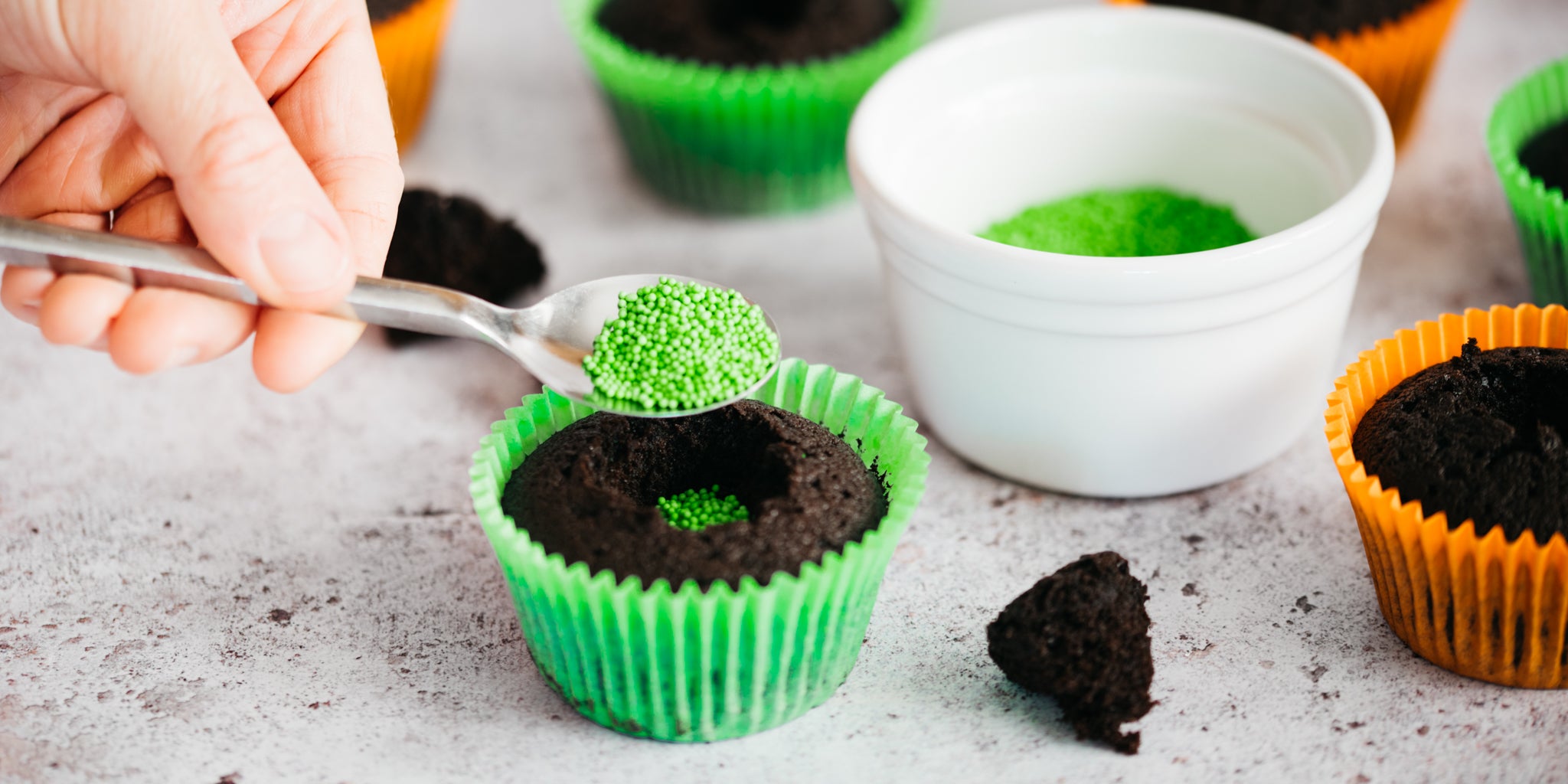Hand spoon green sprinkles into centre of cupcake
