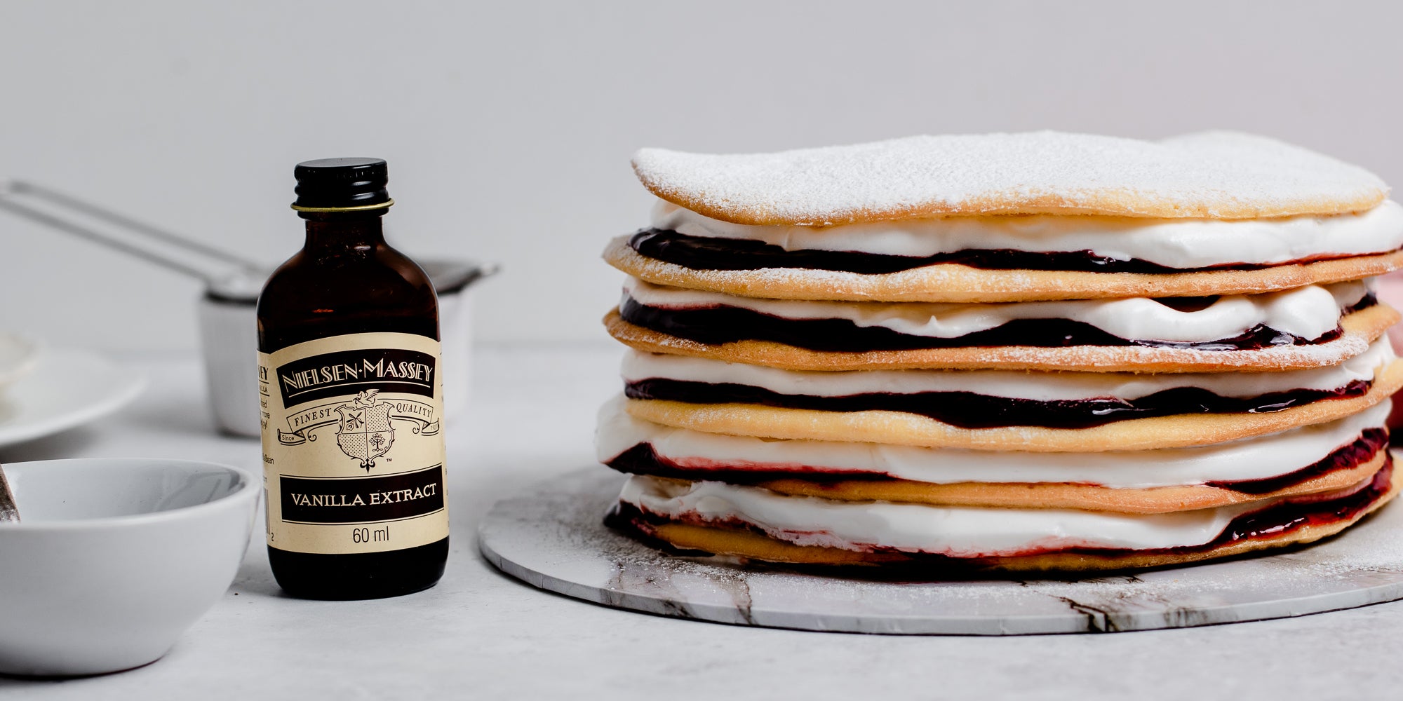 Close up of Danish Layer Cake stacked ontop of a marble serving plate, next to a bottle of Nielsen-Massey Vanilla Extract