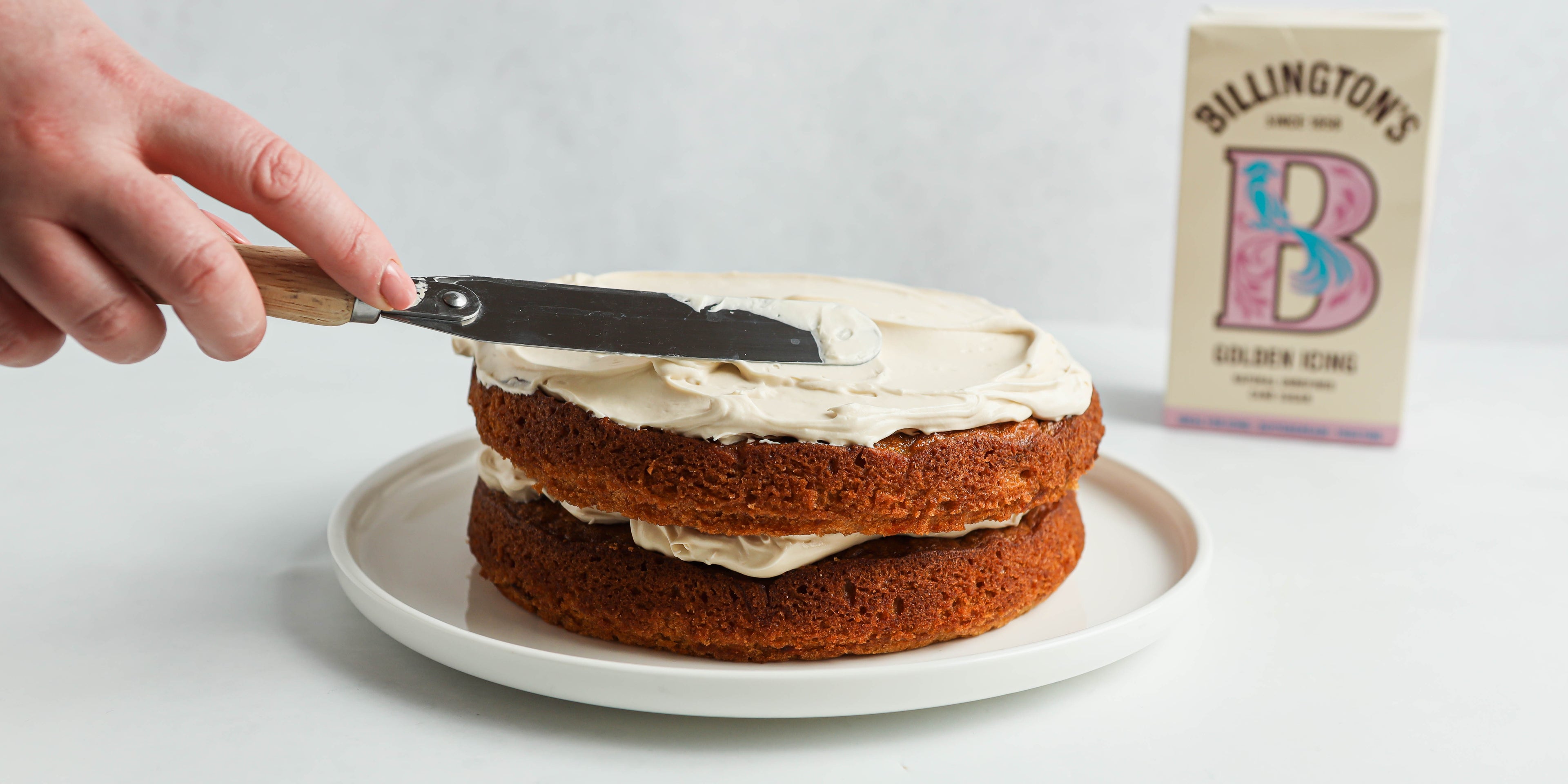 Close up of hand smothering Classic Carrot Cake with Billington's Golden Icing Sugar