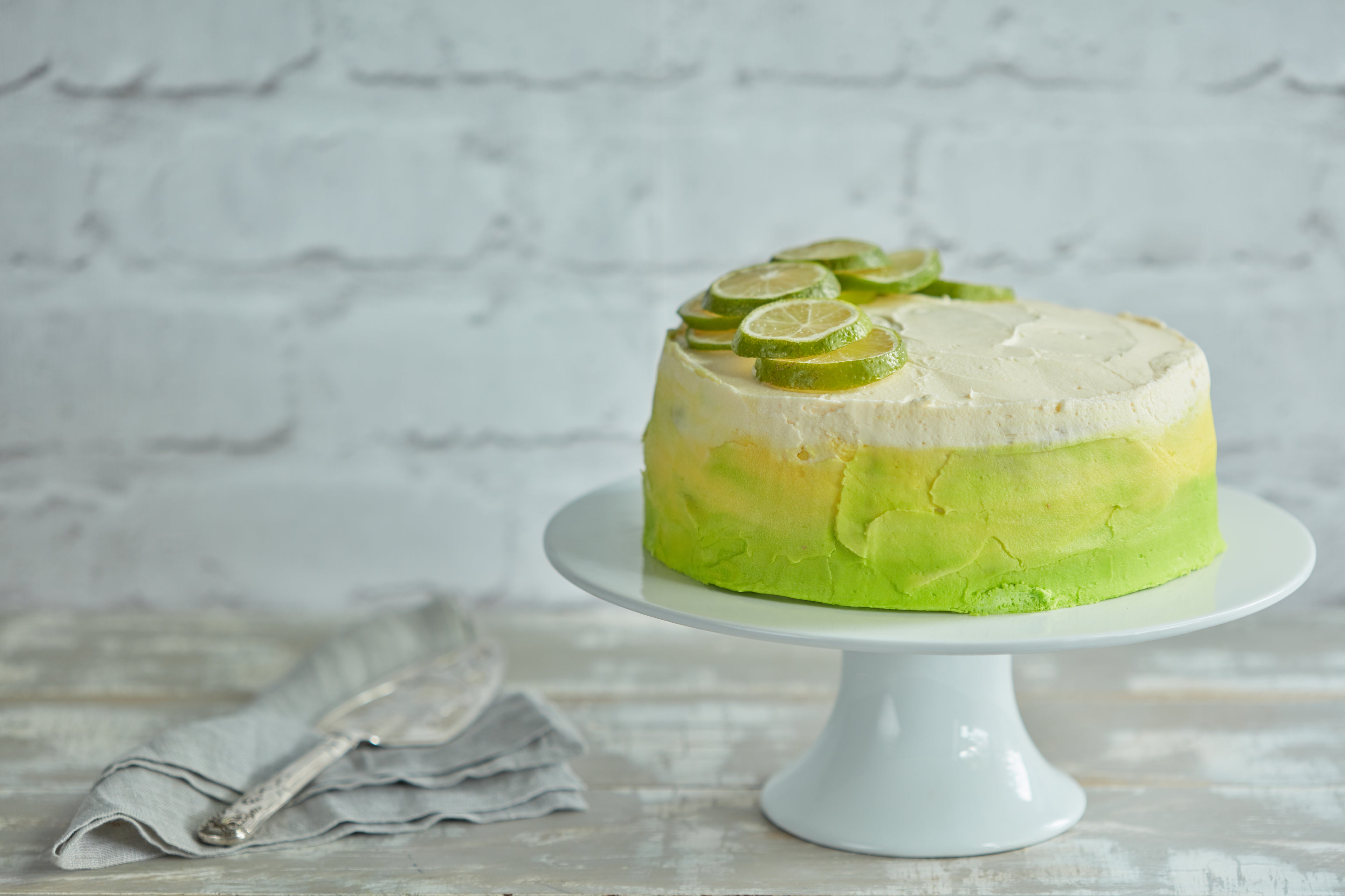 Wide shot of green and wide ombre cake topped with sliced limes on cake stand 