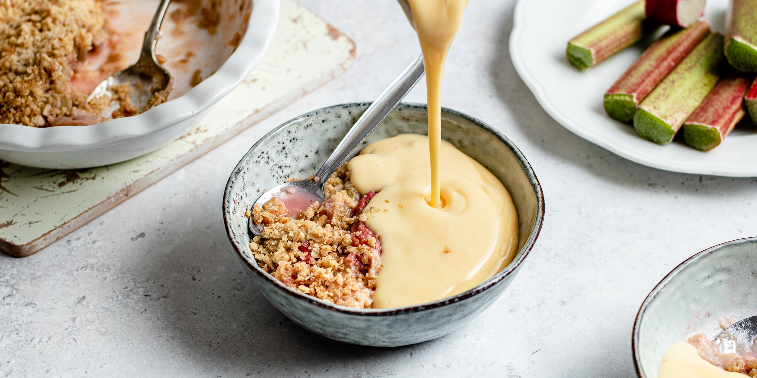 Rhubarb Crumble being poured with warm vanilla custard 