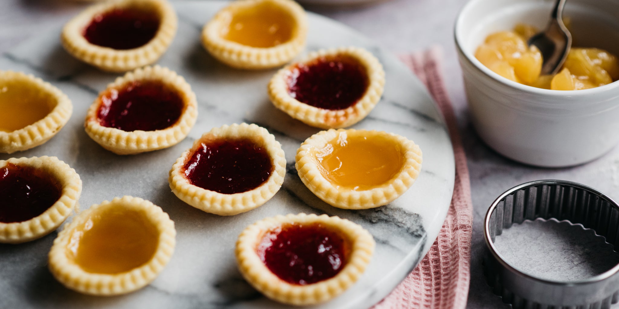 Close up of Strawberry & Apricot Jam Tarts served on a marble board next to a pastry cutter