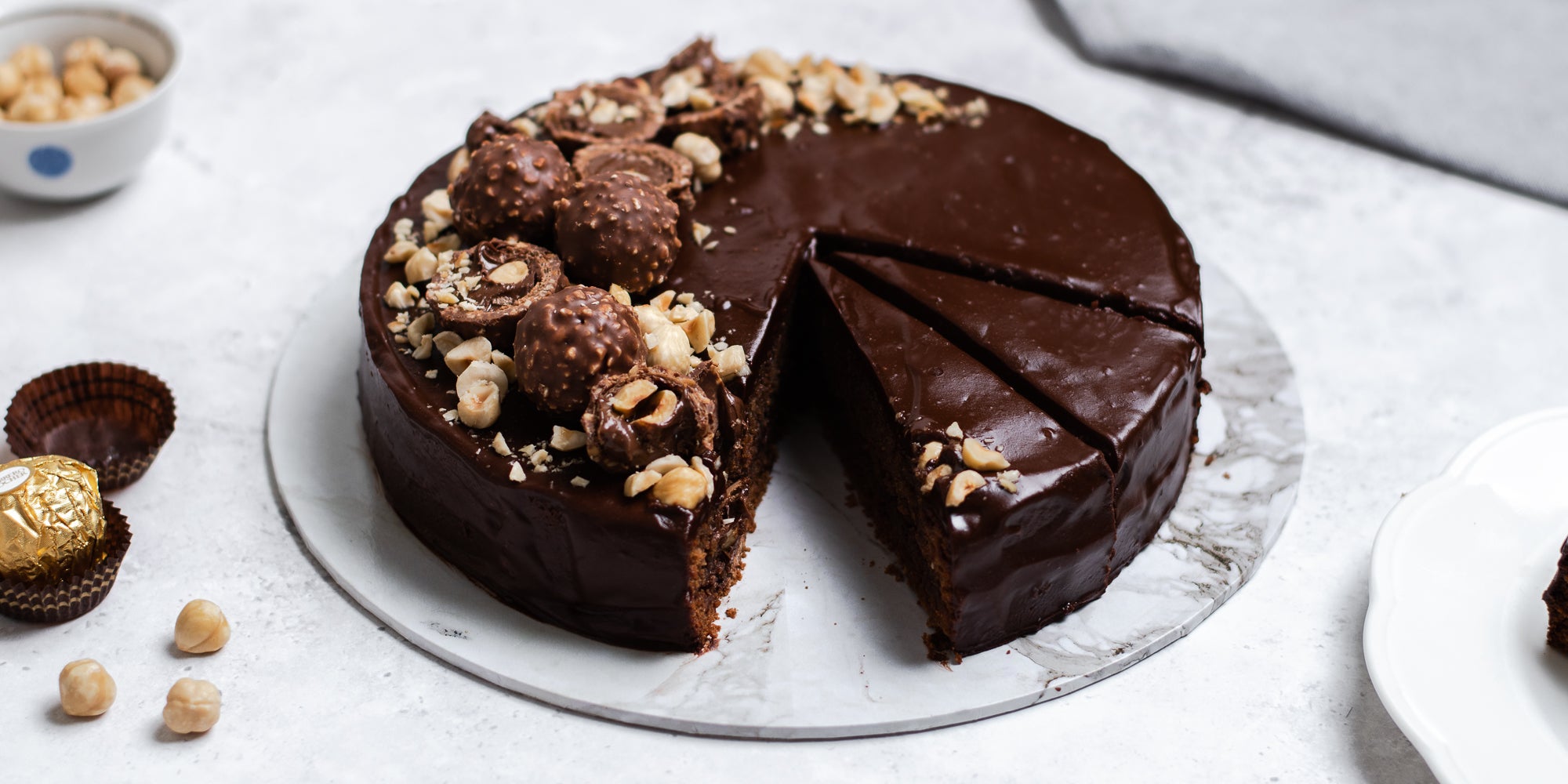 Gluten Free Chocolate Truffle Sachertorte sliced into pieces ready to serve. Sprinkled with hazelnuts served on a marble plate. Bowl of hazelnuts in the background