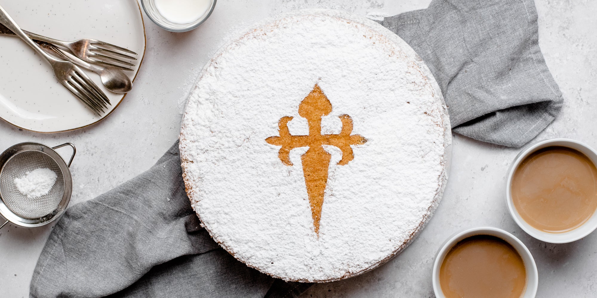 Top view of Tarta de Santiago next to cups of tea, and a plate with forks ready to serve