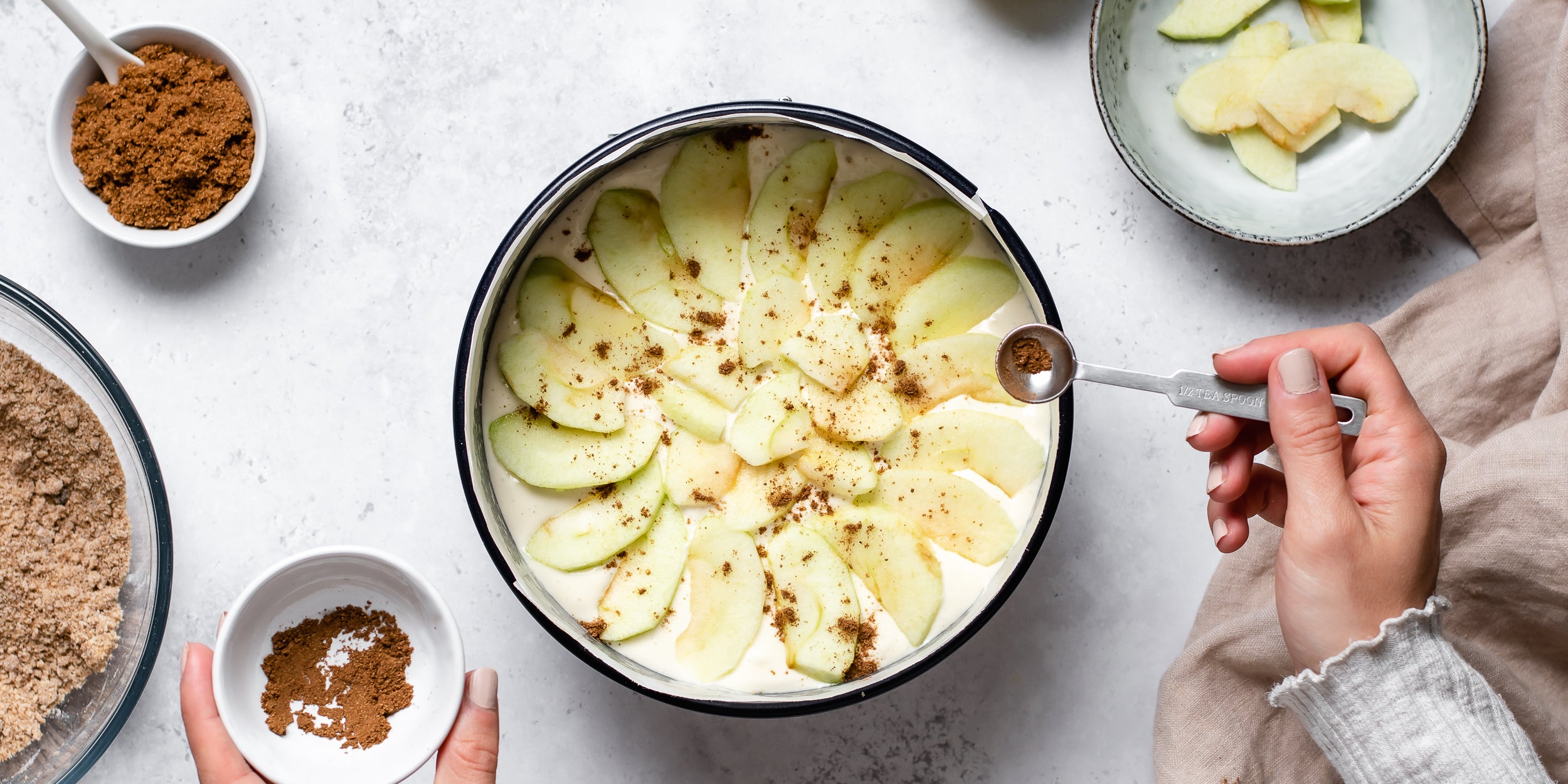 Top view of Apple Crumble Cheesecake being layered up with slice apple and sprinkled cinnamon