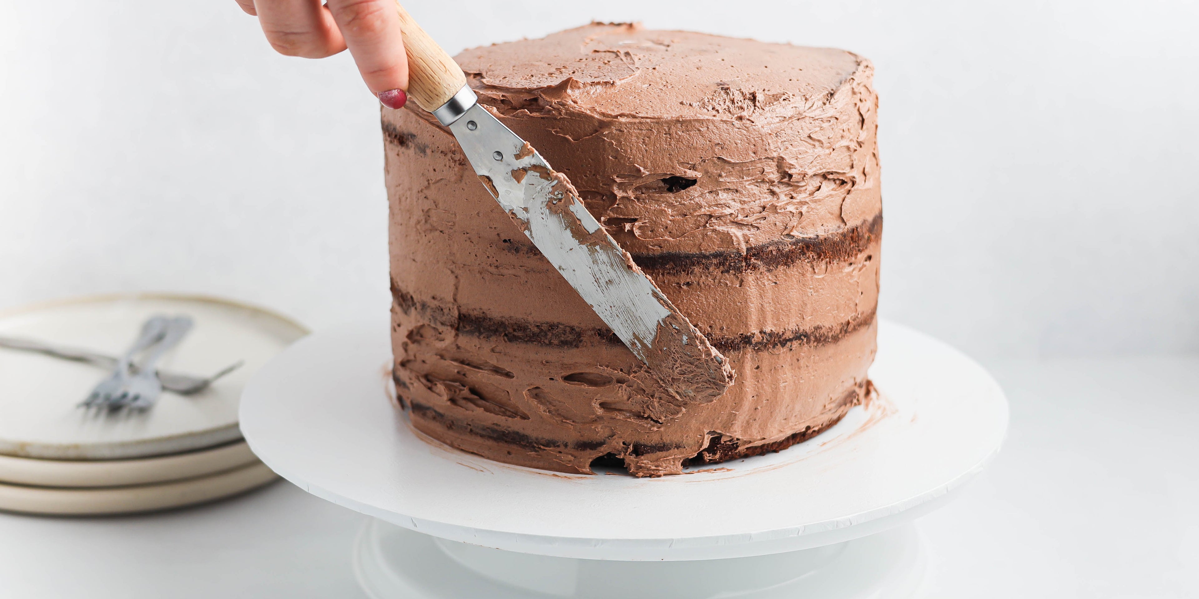 Christmas Reindeer Cake action shot, applying the crumb coat to the chocolate layered cake. Hand using spatula to spread the chocolate buttercream onto the cake.