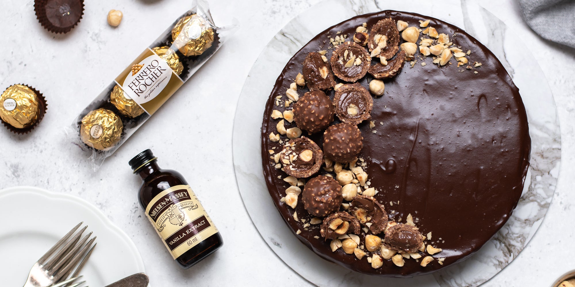 Top view of Gluten Free Chocolate Truffle Sachertorte sprinkled with hazelnuts, next to a packet of Ferrero Rocher's and a bottle of Nielsen-Massey Vanilla Extract