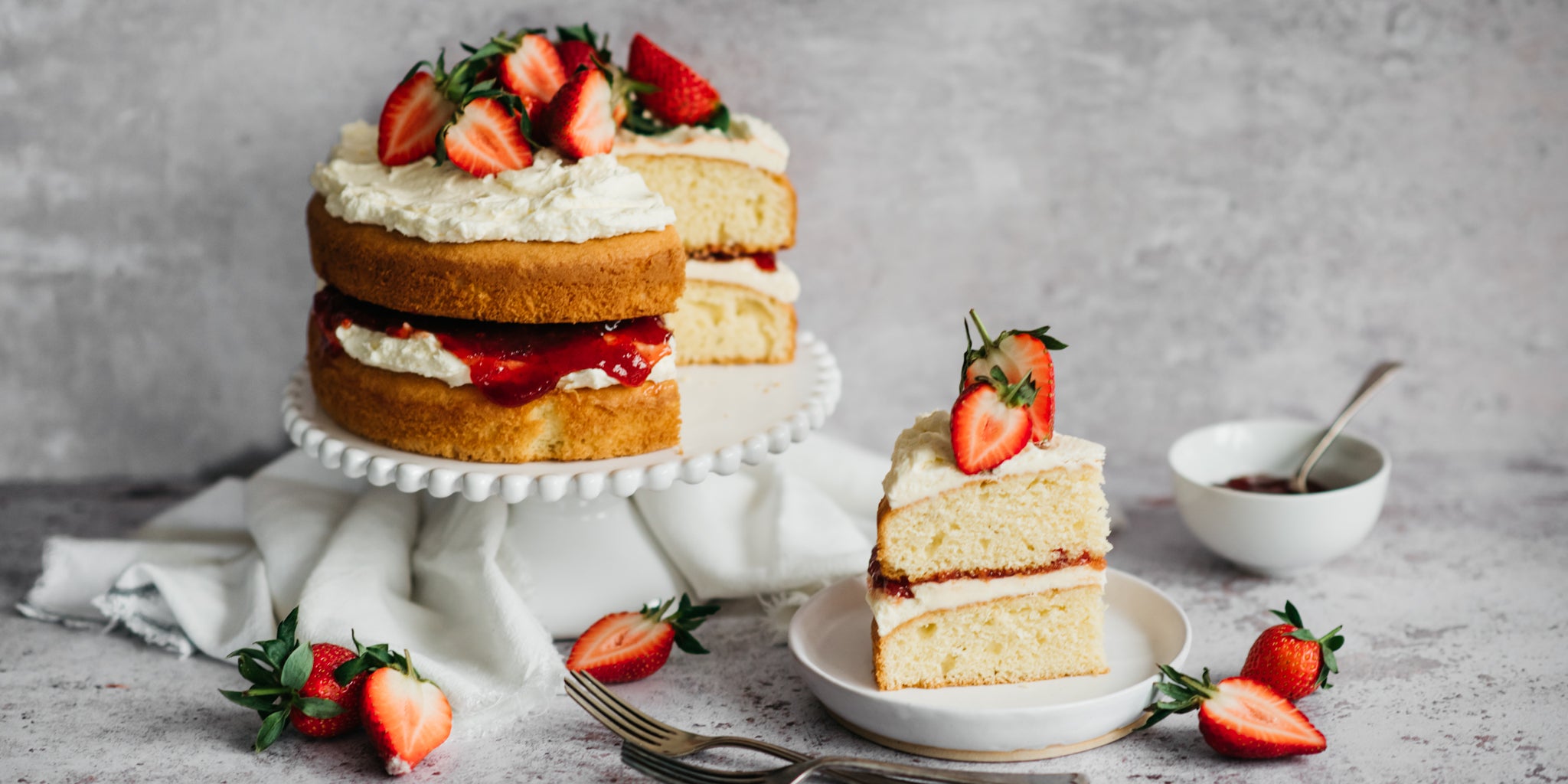 Gluten Free Victoria Sponge served on a cake stand, with a large slice cut out showing the delicious cream and jam filling