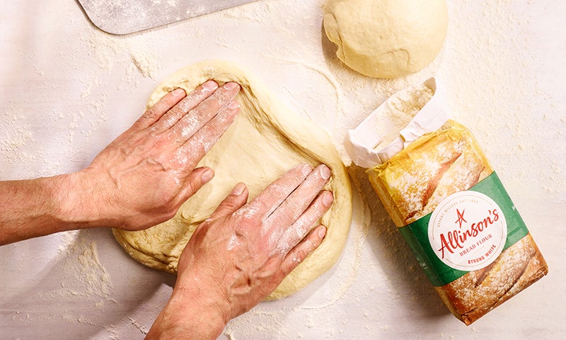 Hands spreading out pizza dough with a pack of flour beside them