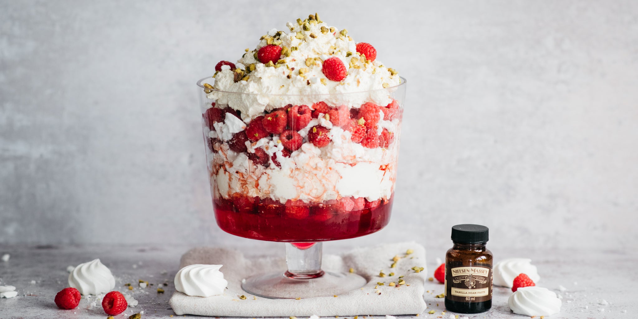 Eton Mess Trifle next to a bottle of Nielsen-Massey vanilla paste and scattered crumbs of meringue and chopped nuts