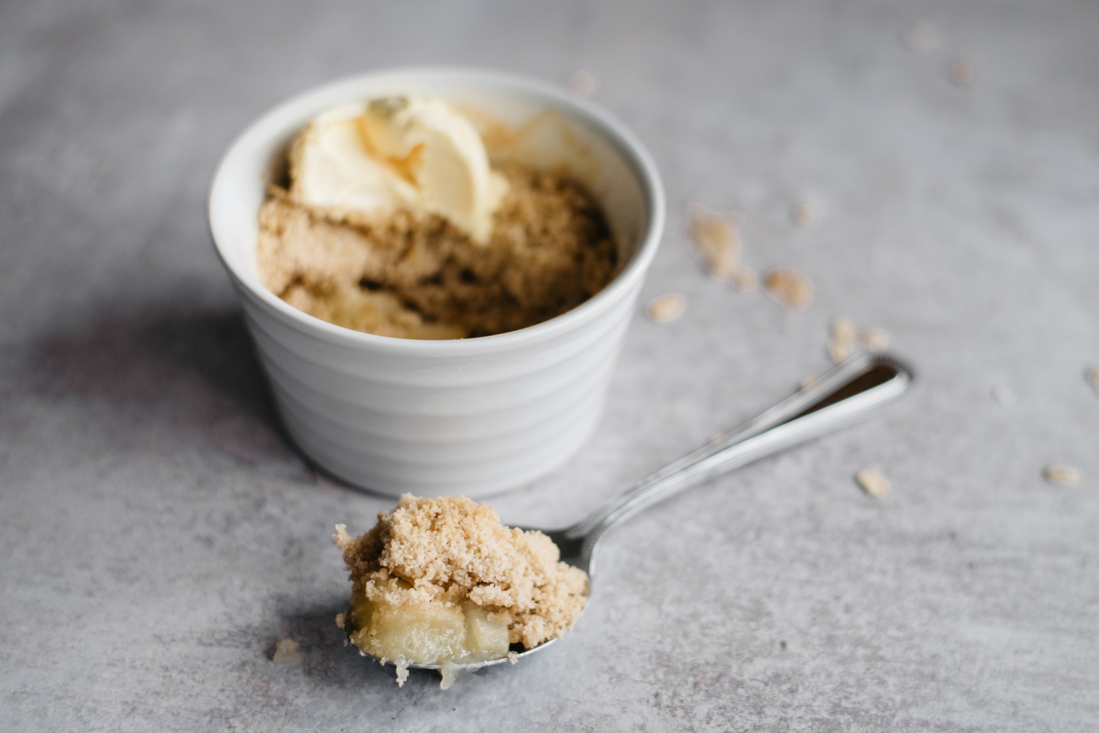 Close up of Mini Apple & Cinnamon Crumble with a spoon dipped into is showing the apple filling, and crunchy crumble topping