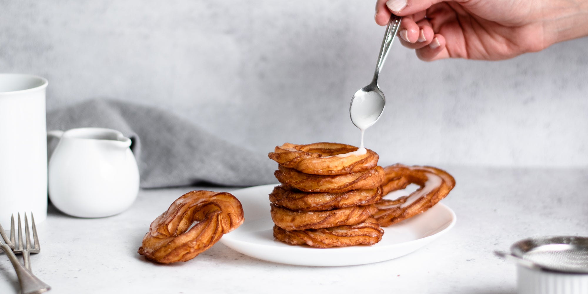 Stack of Apple Cider Crullers being drizzled with Icing with a hand holding a spoon