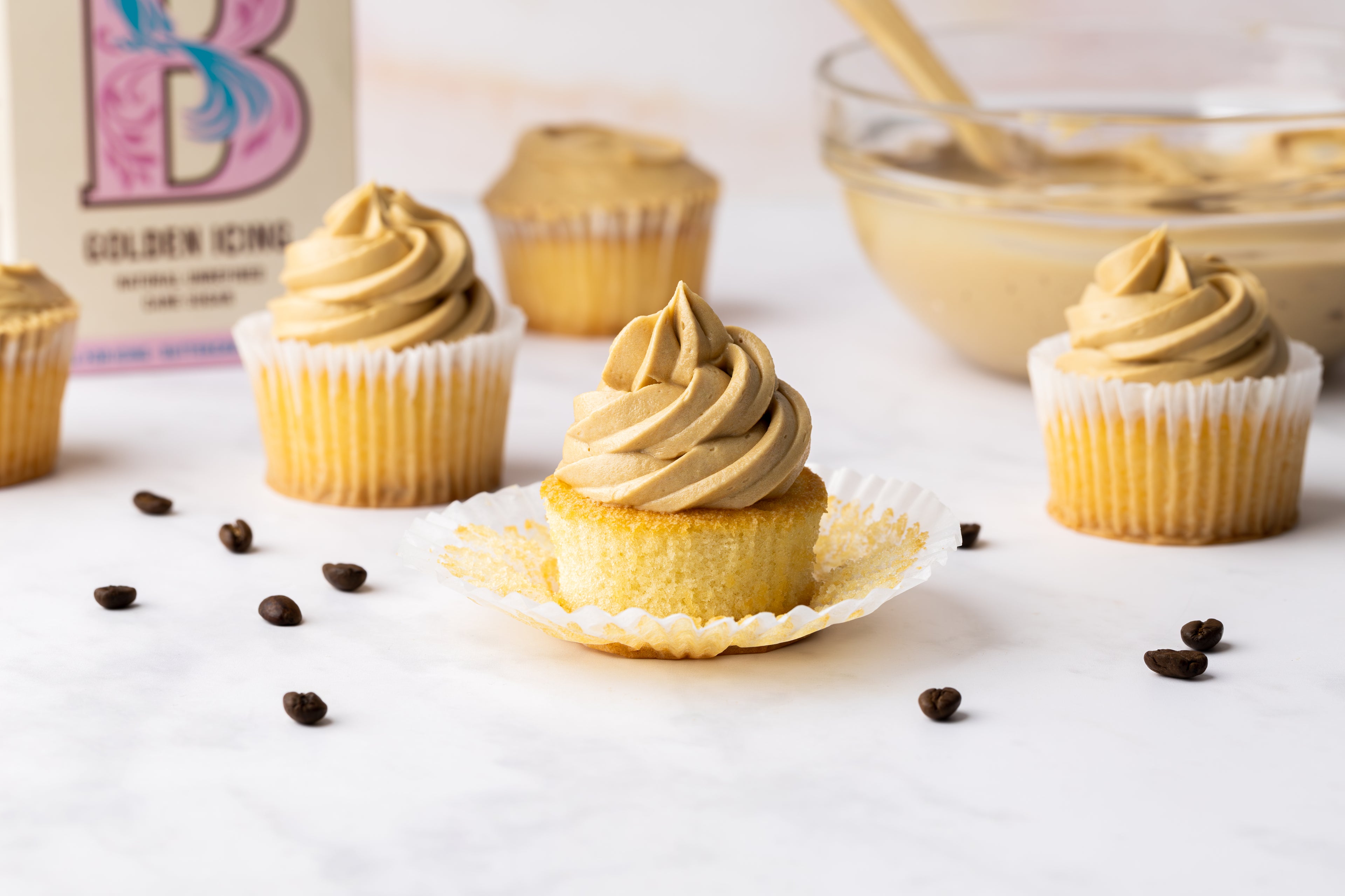 Coffee buttercream covered cupcakes in a line infront of a pack of sugar