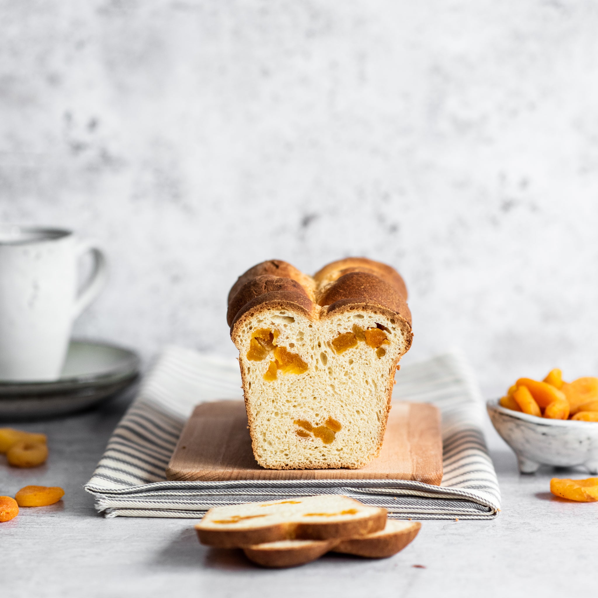 Brioche loaf with two slices cut in front, cup in background and pot of apricots