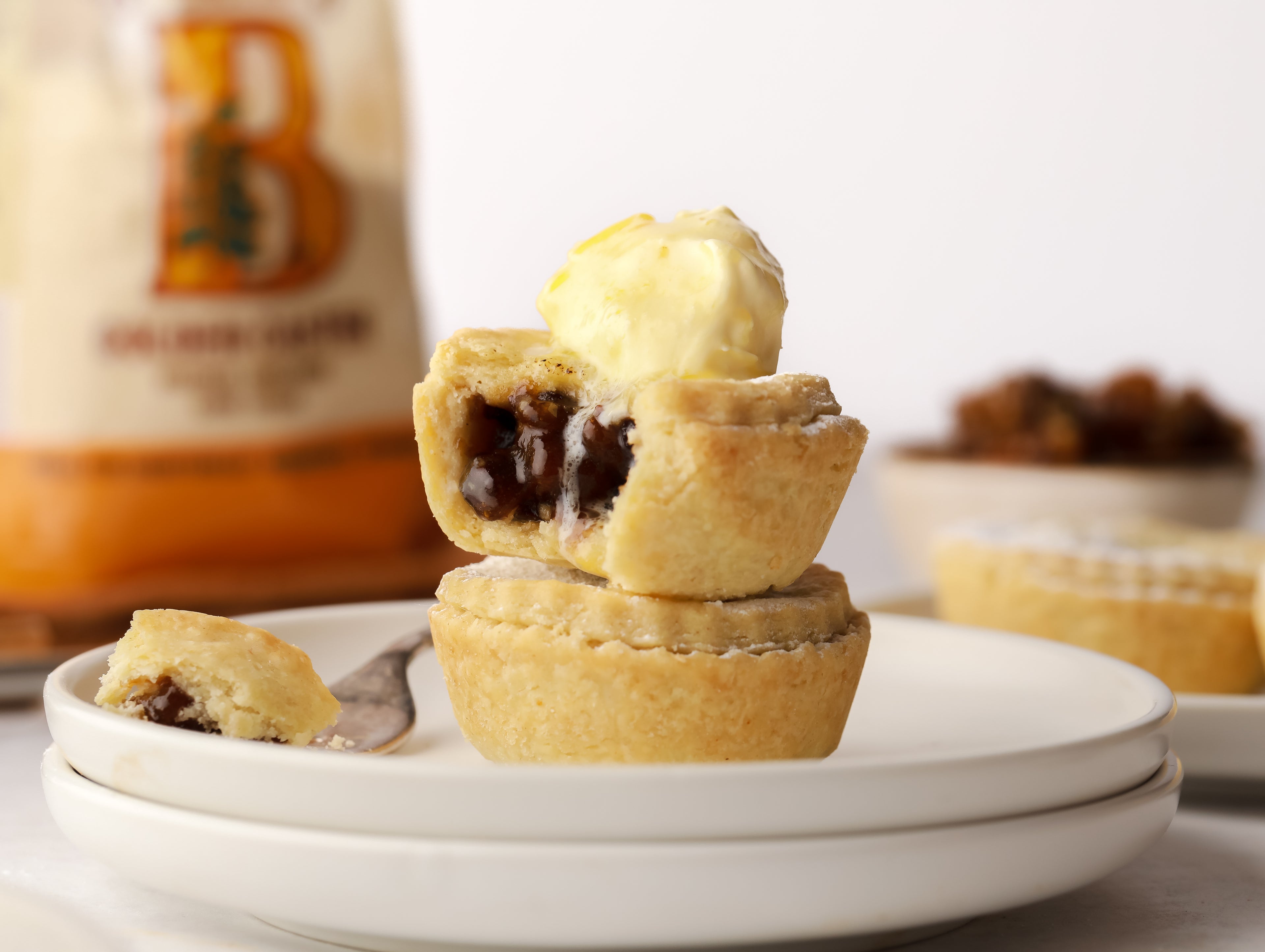 Mince pie with bite taken out stacked on top of another mince pie with brandy butter on top.