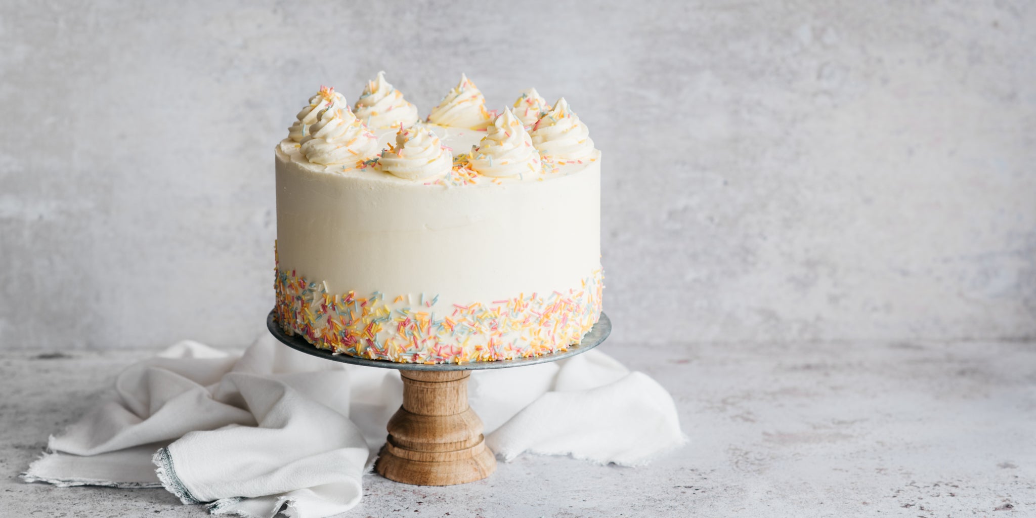 Vegan Vanilla Cake on a cake stand, decorated for a birthday with sprinkles around the base of the vanilla icing 