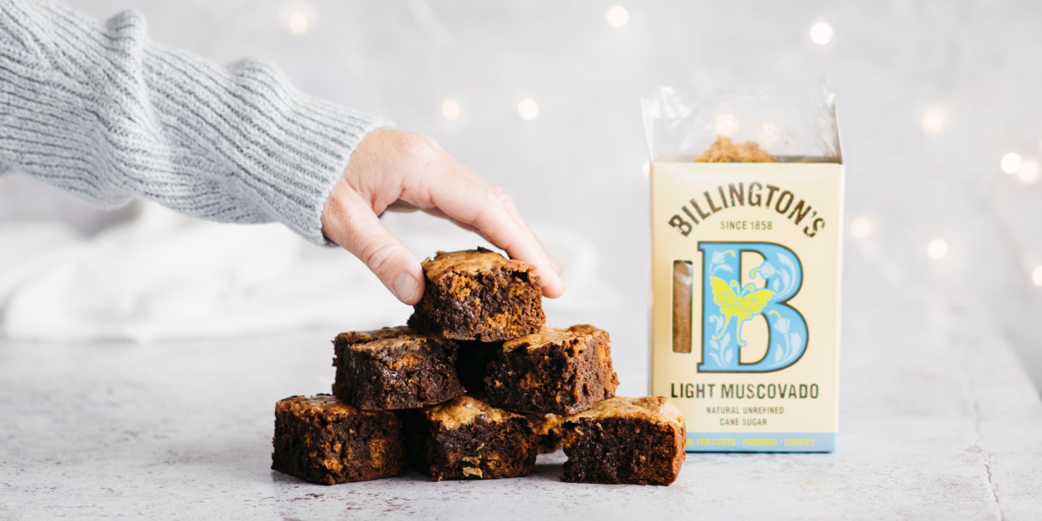 Hand reaching in to take a brownie from the top of a pile. Open sugar pack beside it