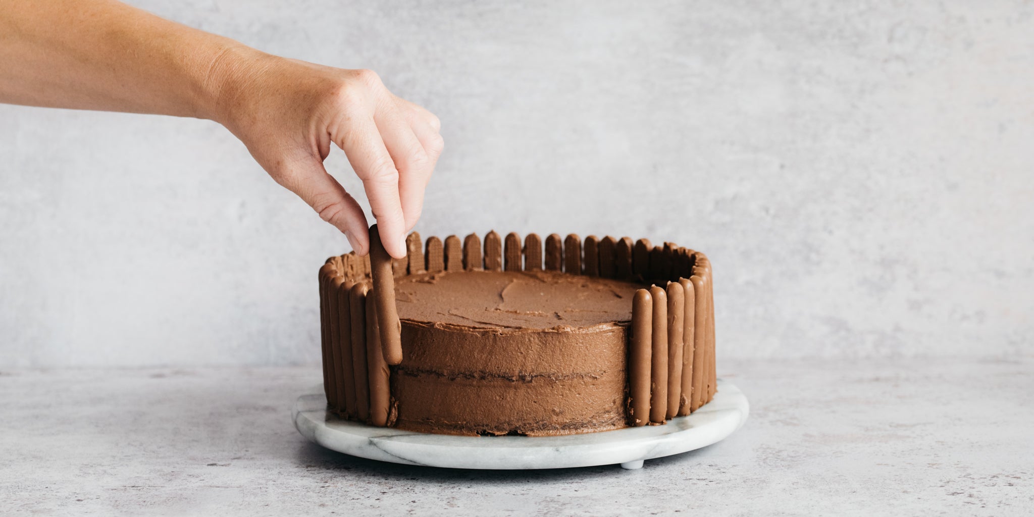 Chocolate Showstopper Cake being hand decorated with chocolate fingers around the edge of the cake