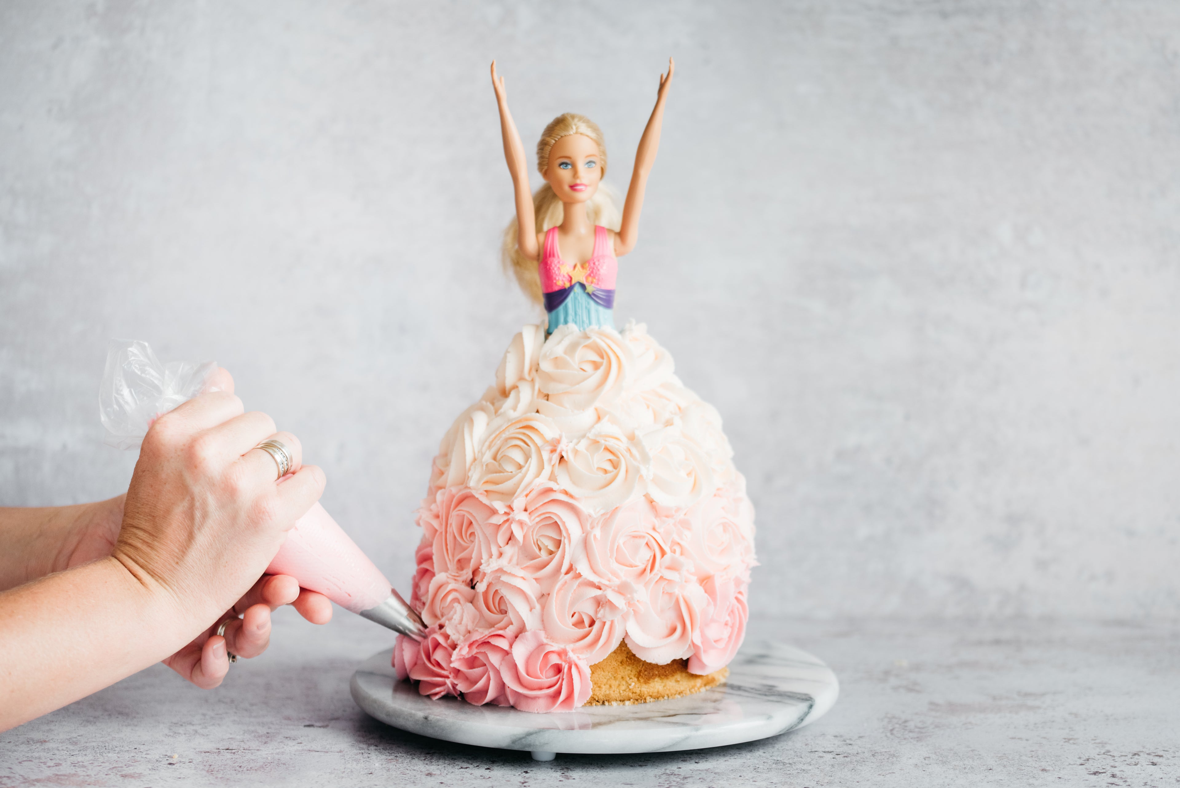 Princess Barbie Cake being hand swirled with pink and white buttercream to decorate the dress section of the cake