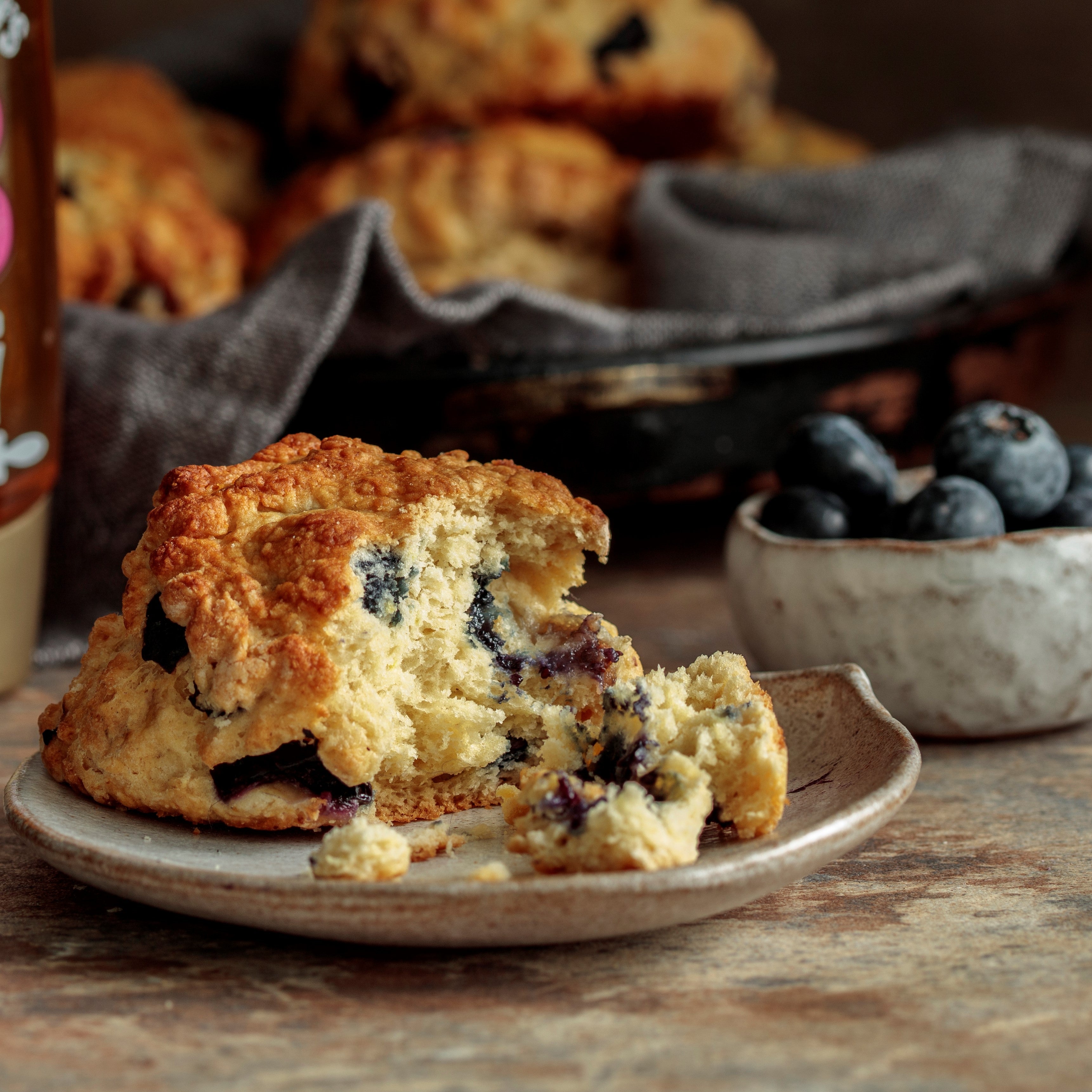 Blueberry honey scone on plate torn open with bowl of blueberries