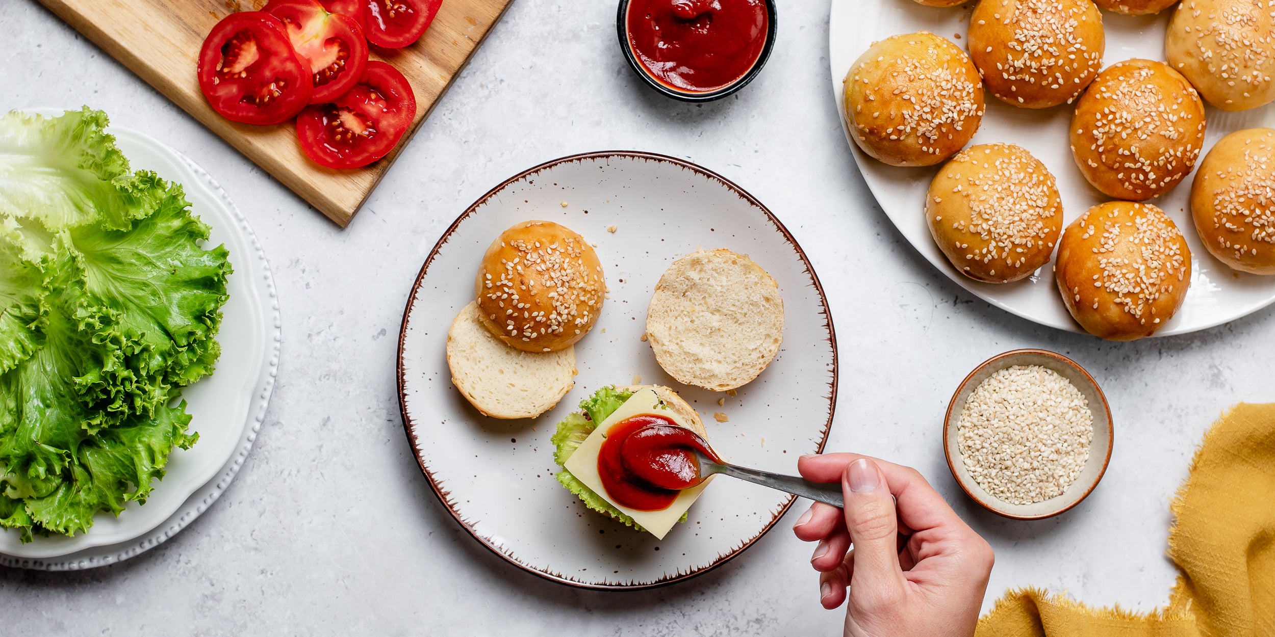 Hand dolloping tomato sauce on top of burger buns 