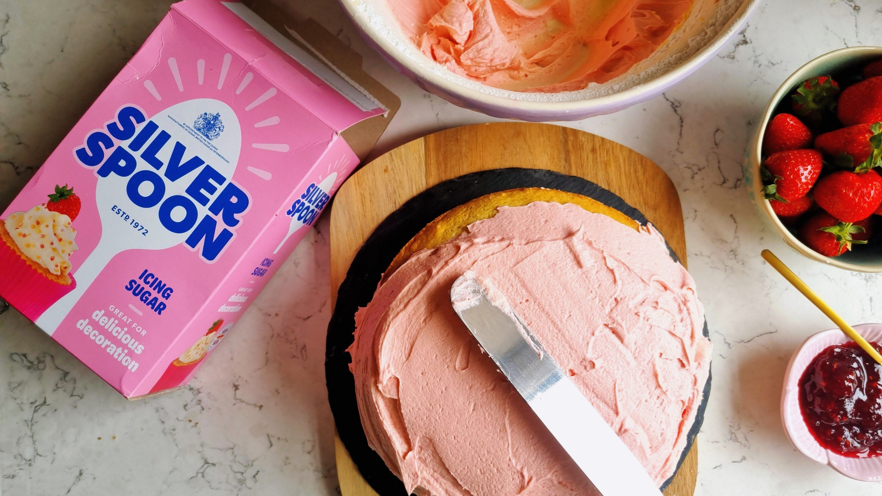 Spreading pink strawberry-flavoured buttercream over a homemade sponge cake