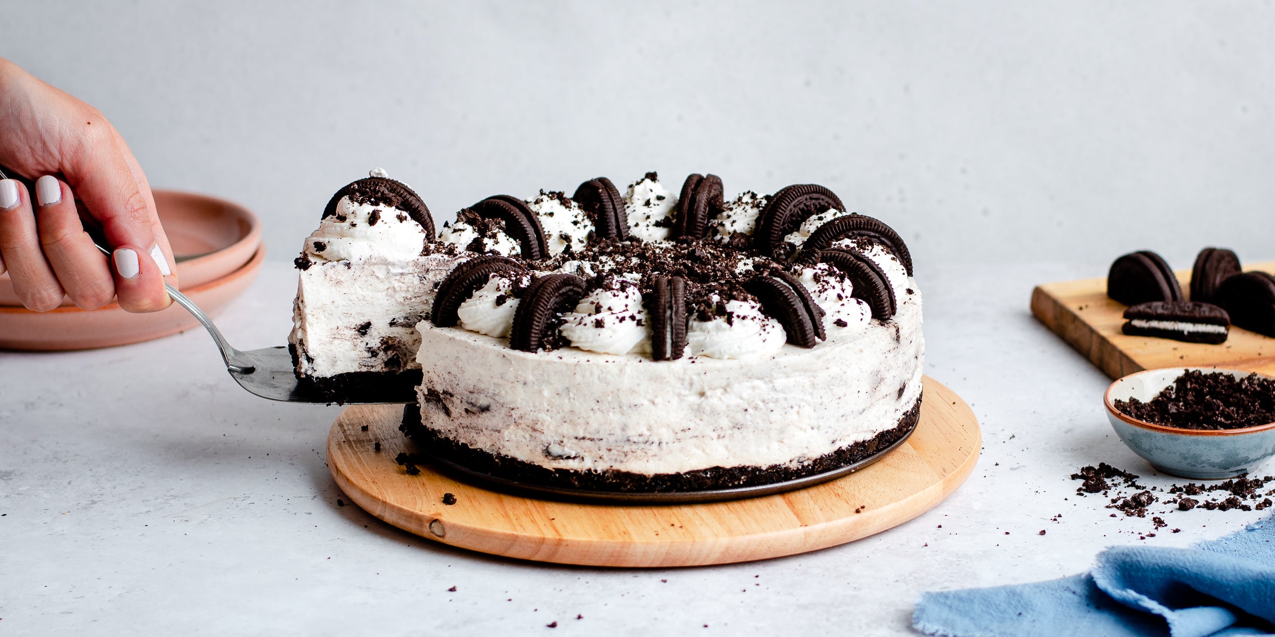 Slice being taken from no-bake Oreo cheesecake on a wooden plate