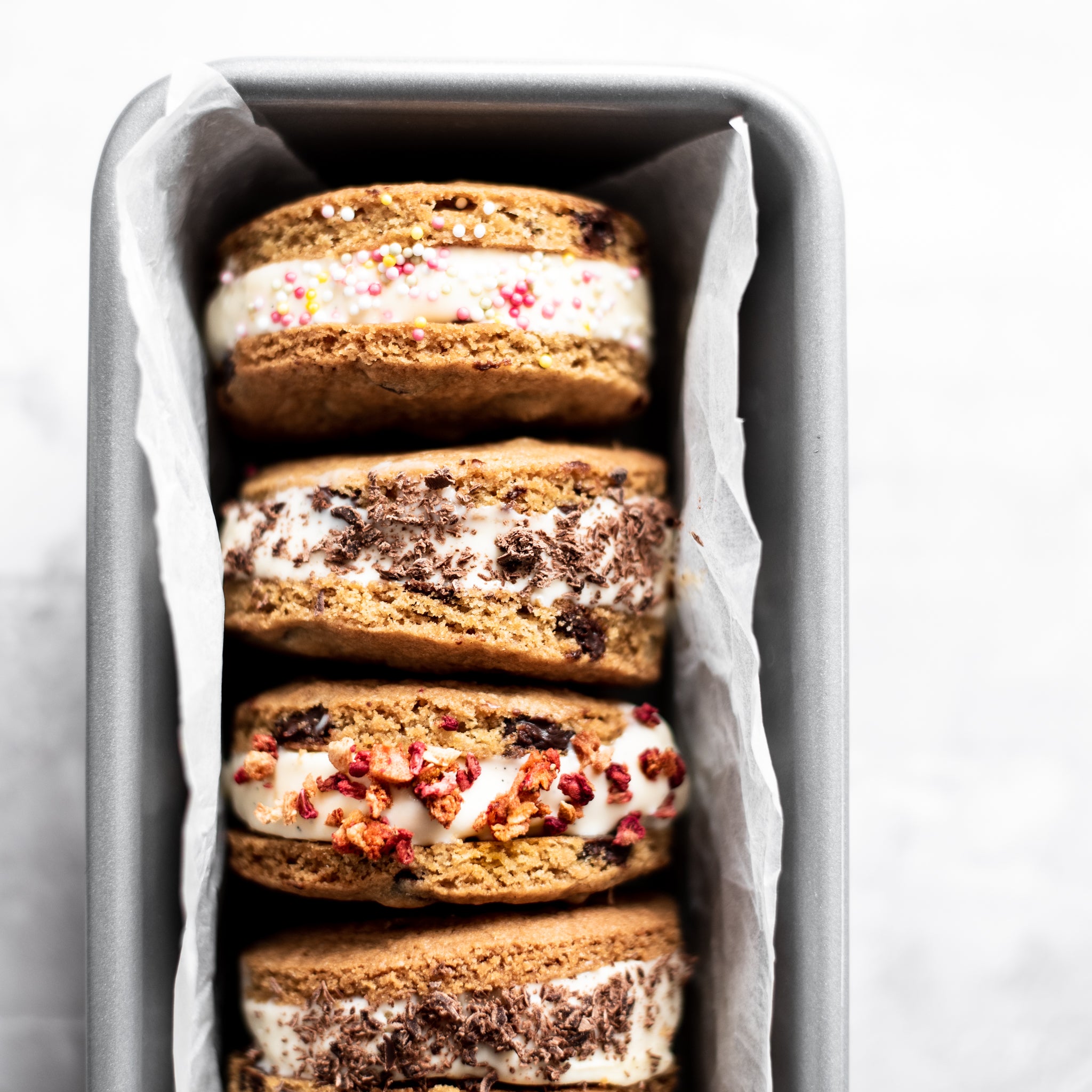 Close-up of four ice cream cookie sandwiches, sprinkled with different toppings