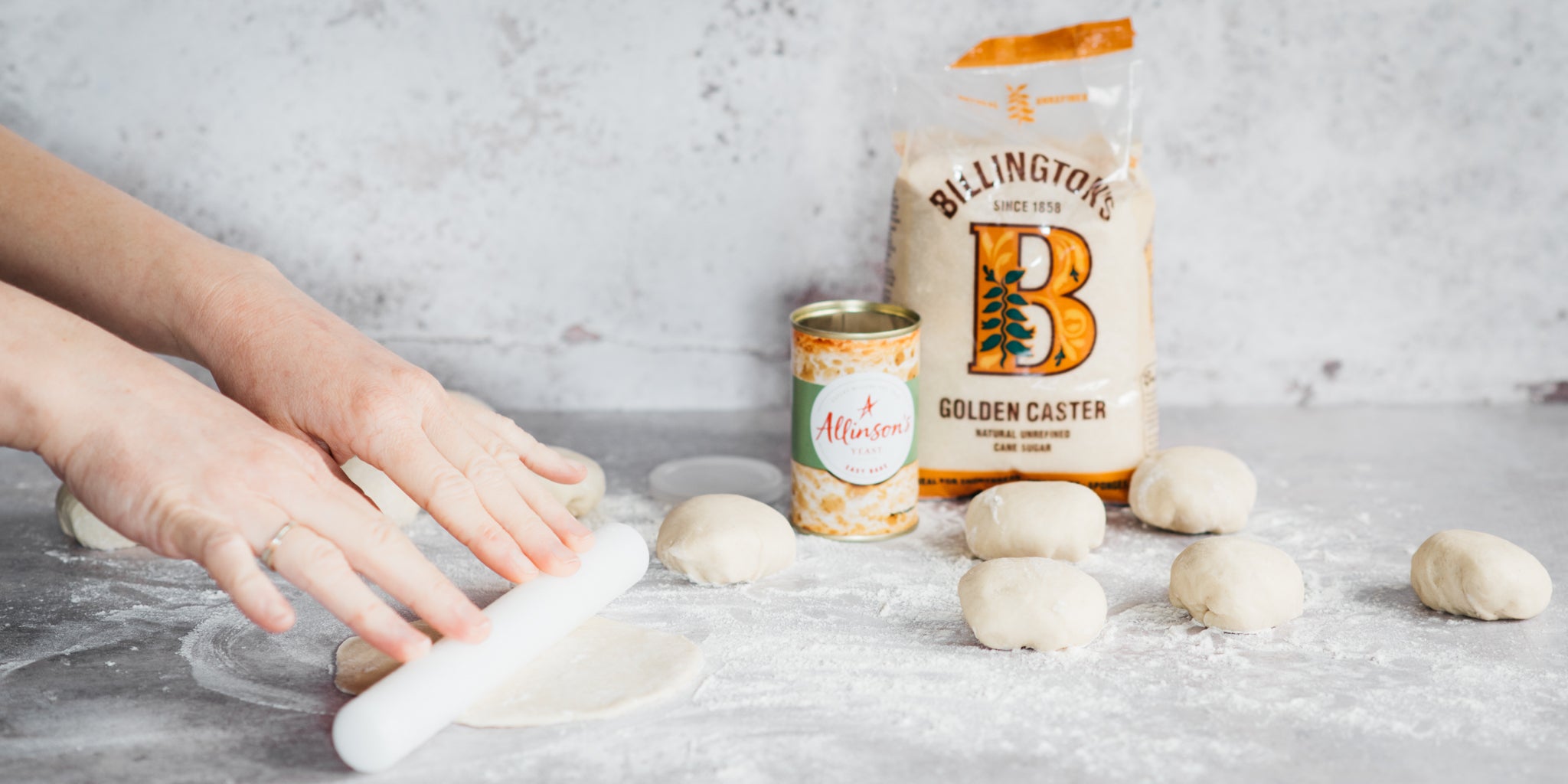 Hands rolling out bao bun dough and tin of yeast and sugar in background