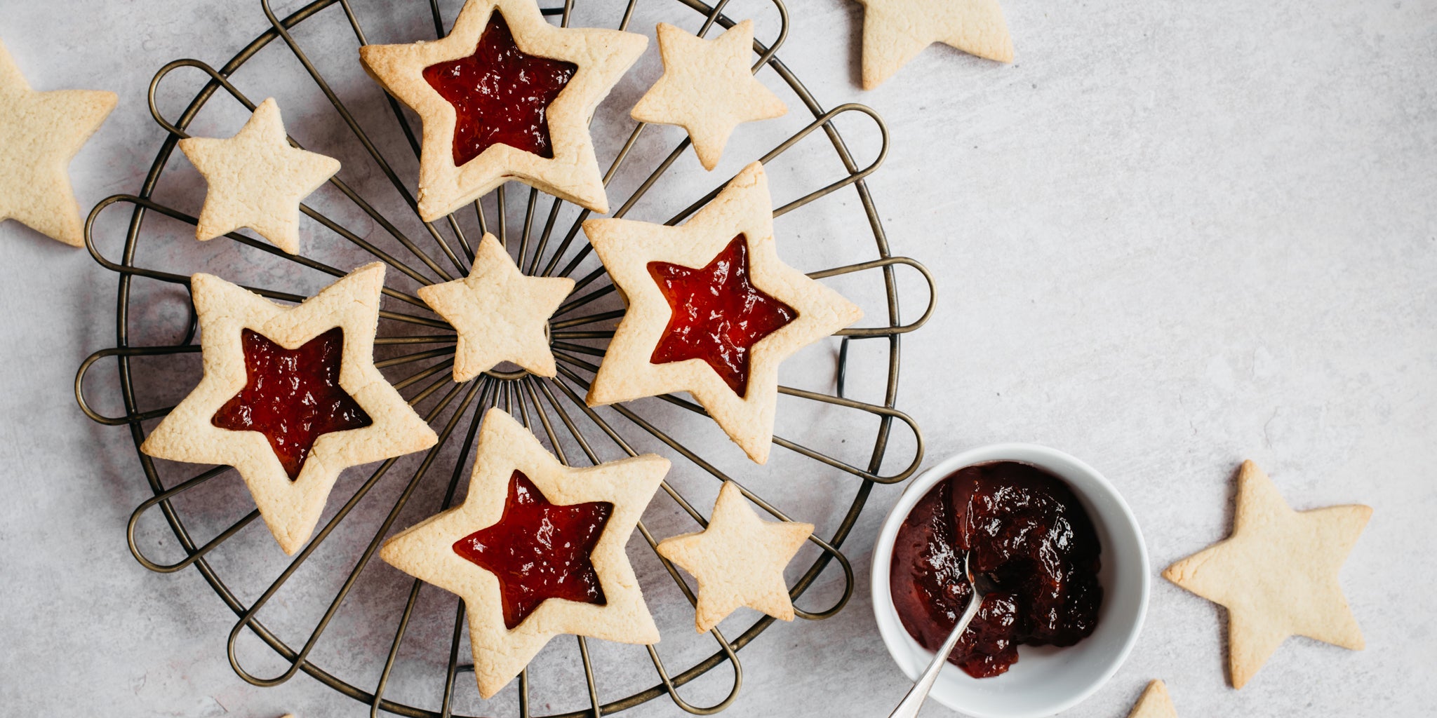 Top down shot of vanilla biscuits filled with jam on a cooling rack. A small bowl of jam with a spoon is next to it