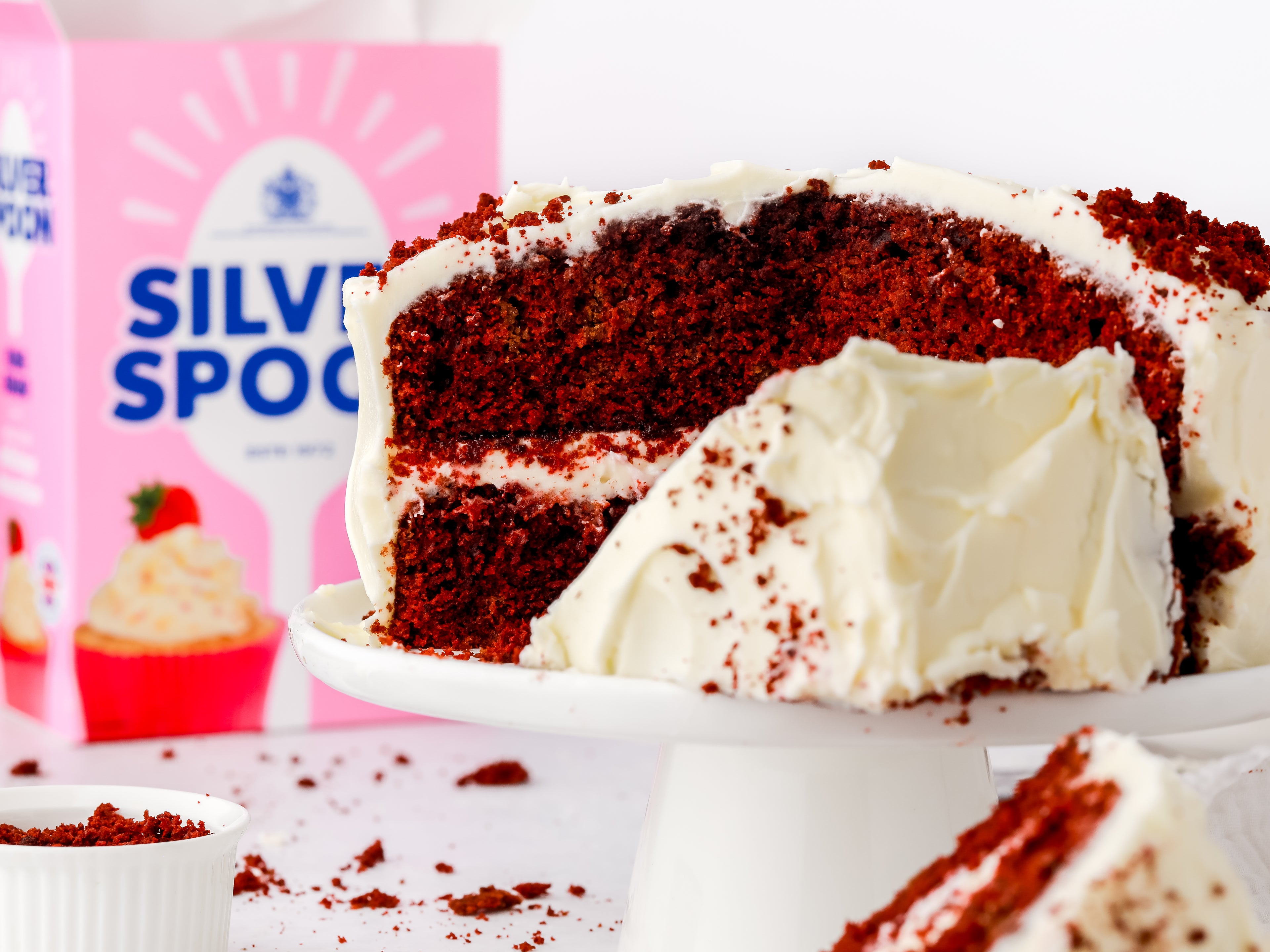 Cut red velvet cake on a cake stand in front of a pack of icing sugar