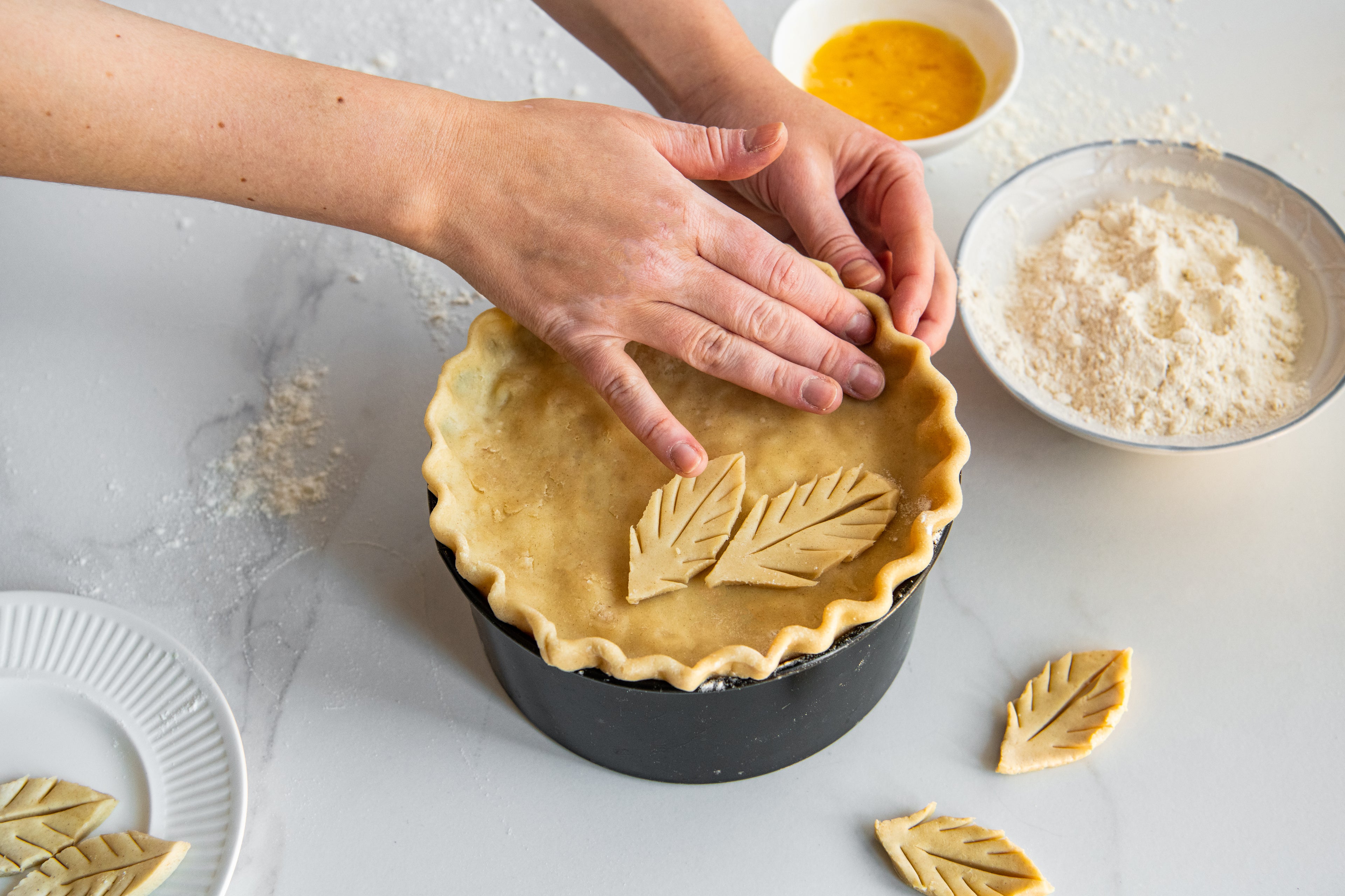 Turkey, Ham & Leek Pie being prepared by hands pushing the pastry on top next to a bowl of flour