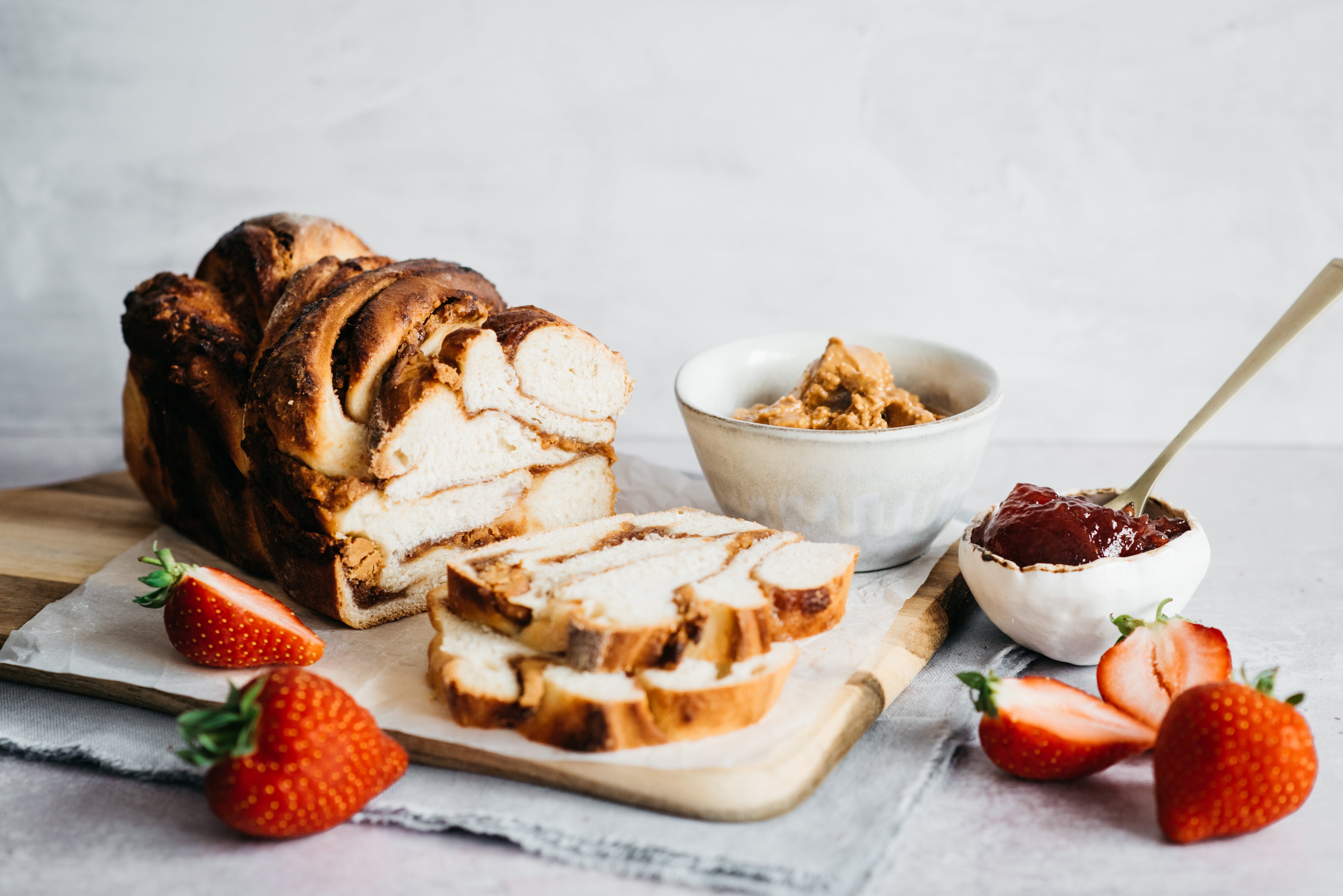 Peanut Butter Jam Babka on baking paper with chopped strawberries and choice of spreads