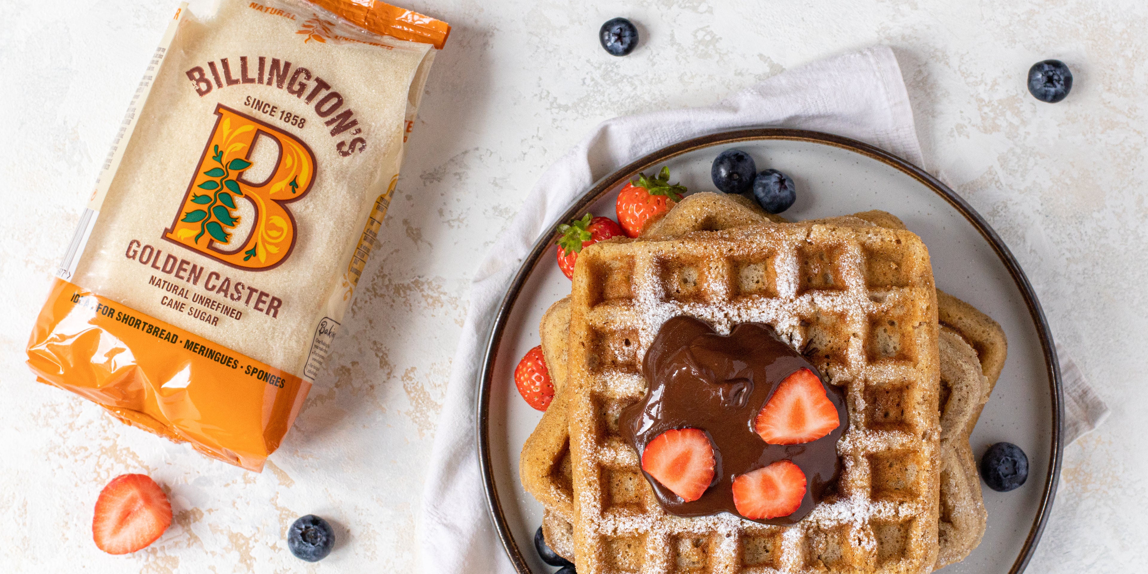 Stack of Waffles topped with chocolate and strawberries, next to a bag of Billington's Golden Caster sugar
