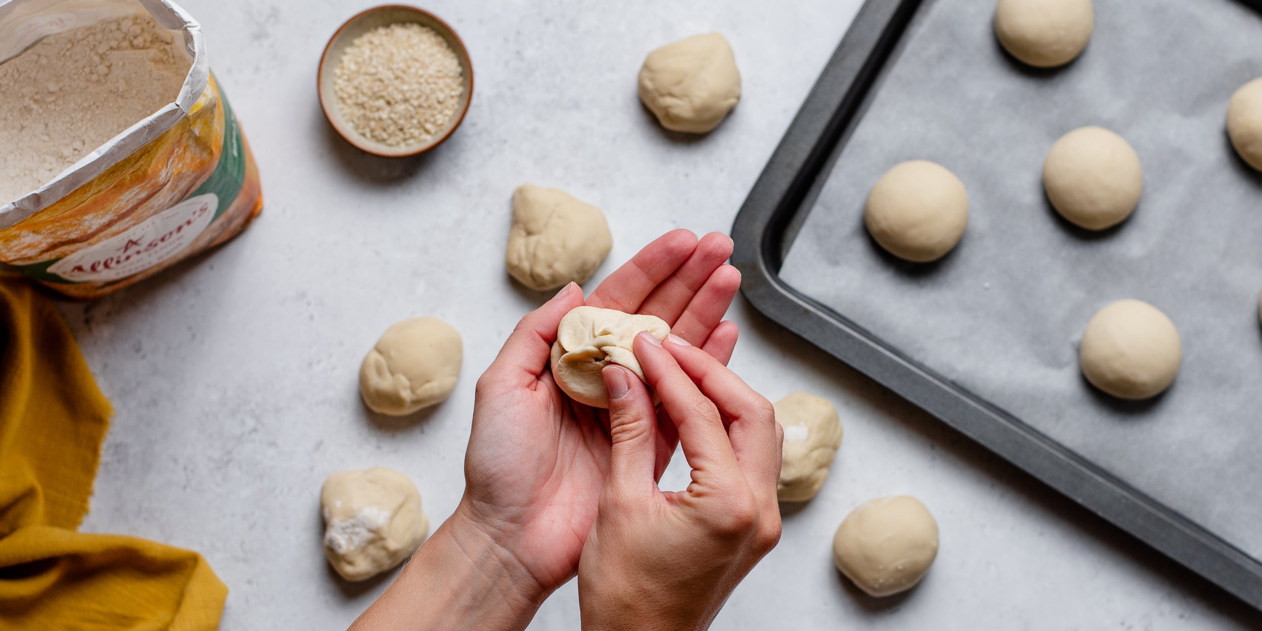 Hands rolling small balls of bread dough and a baking tray in the background