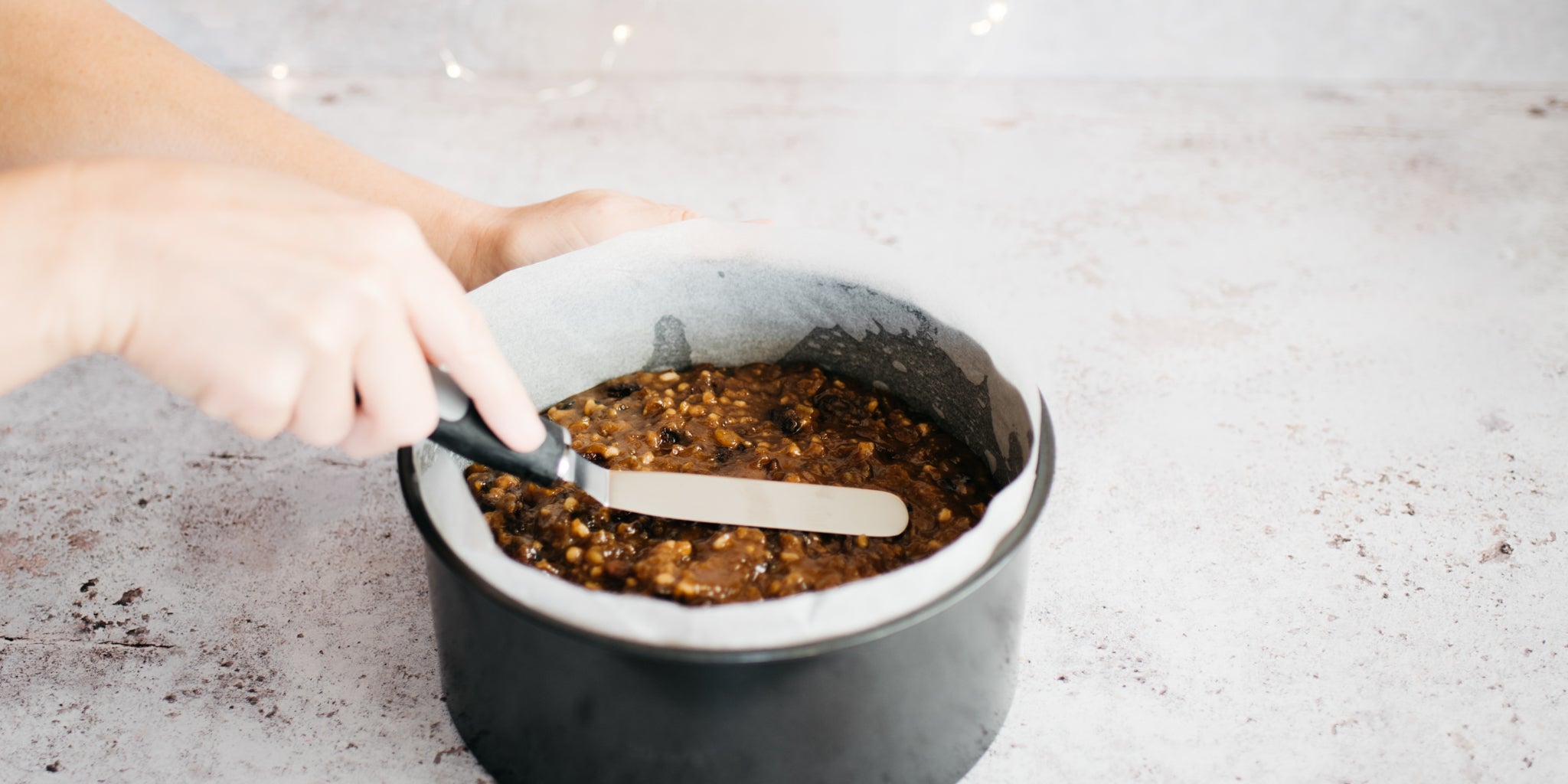 Smoothing down a Christmas cake mixture inside a metal cake tin