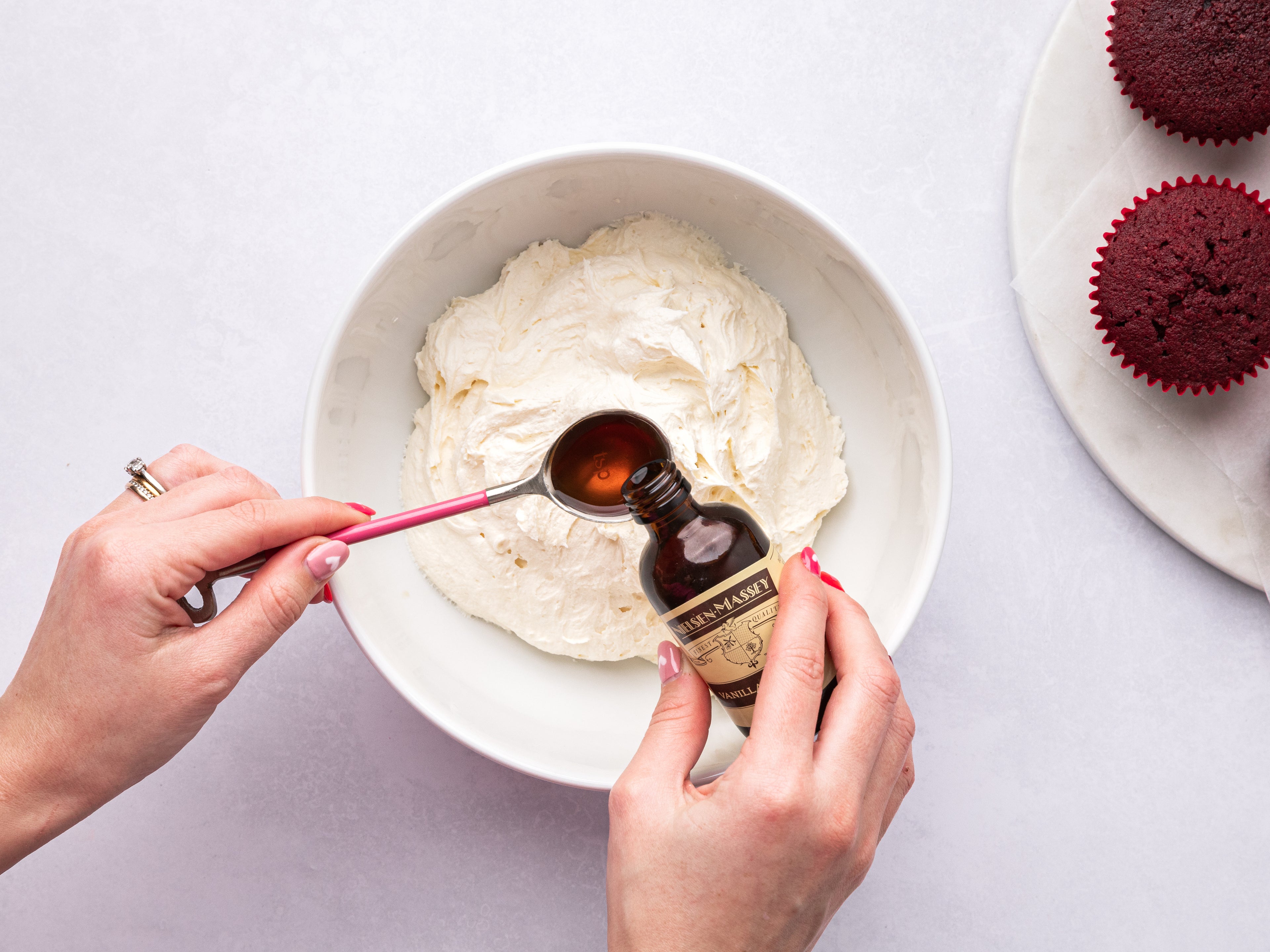 Hands measuring out a teaspoon of vanilla extract into a bowl of buttercream