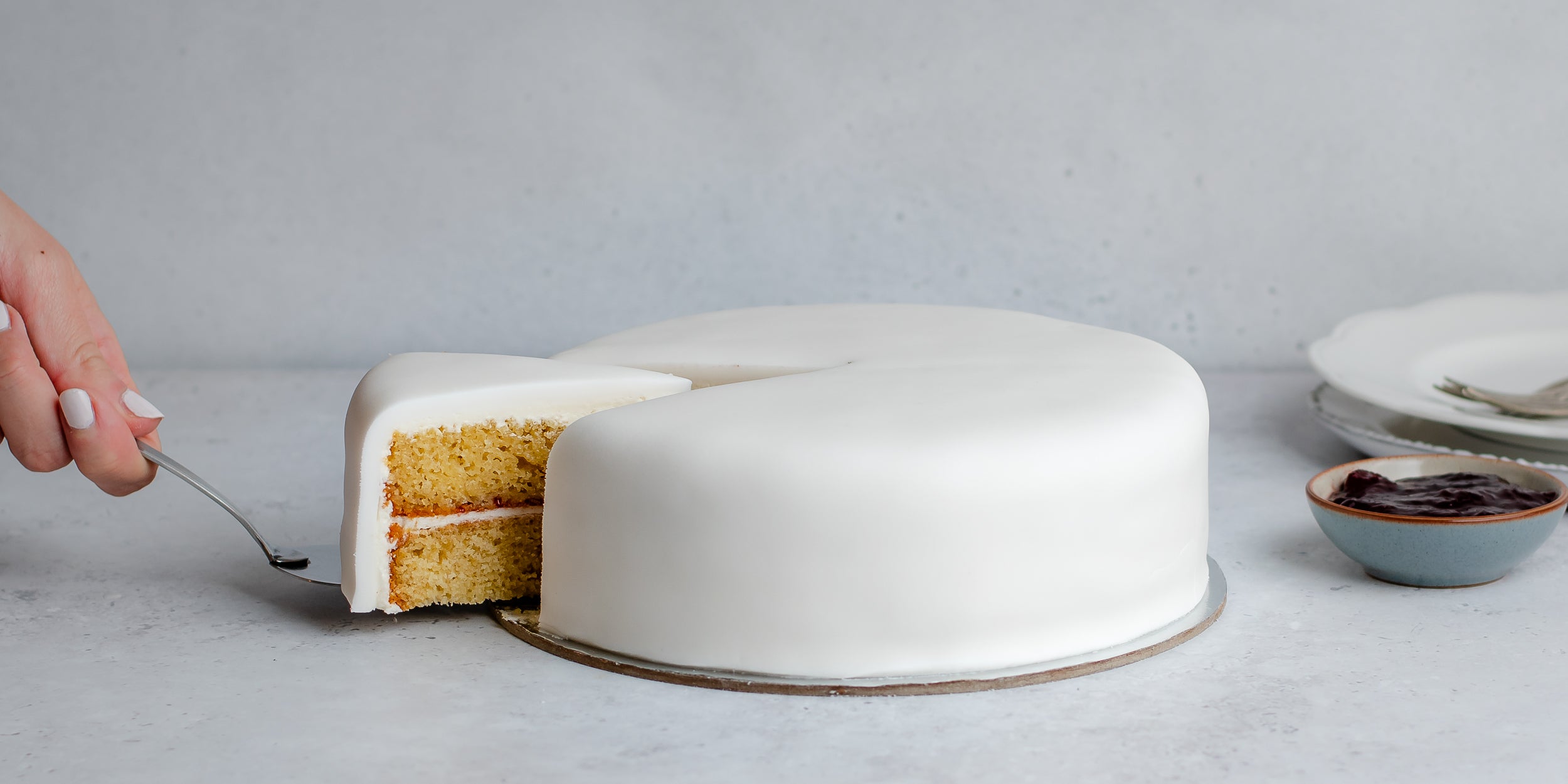 White fondant covered cake with hand to leave removed a slice with a cake knife