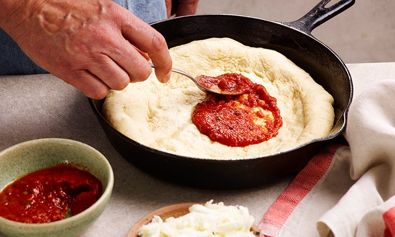 Spreading tomato sauce across a pizza base