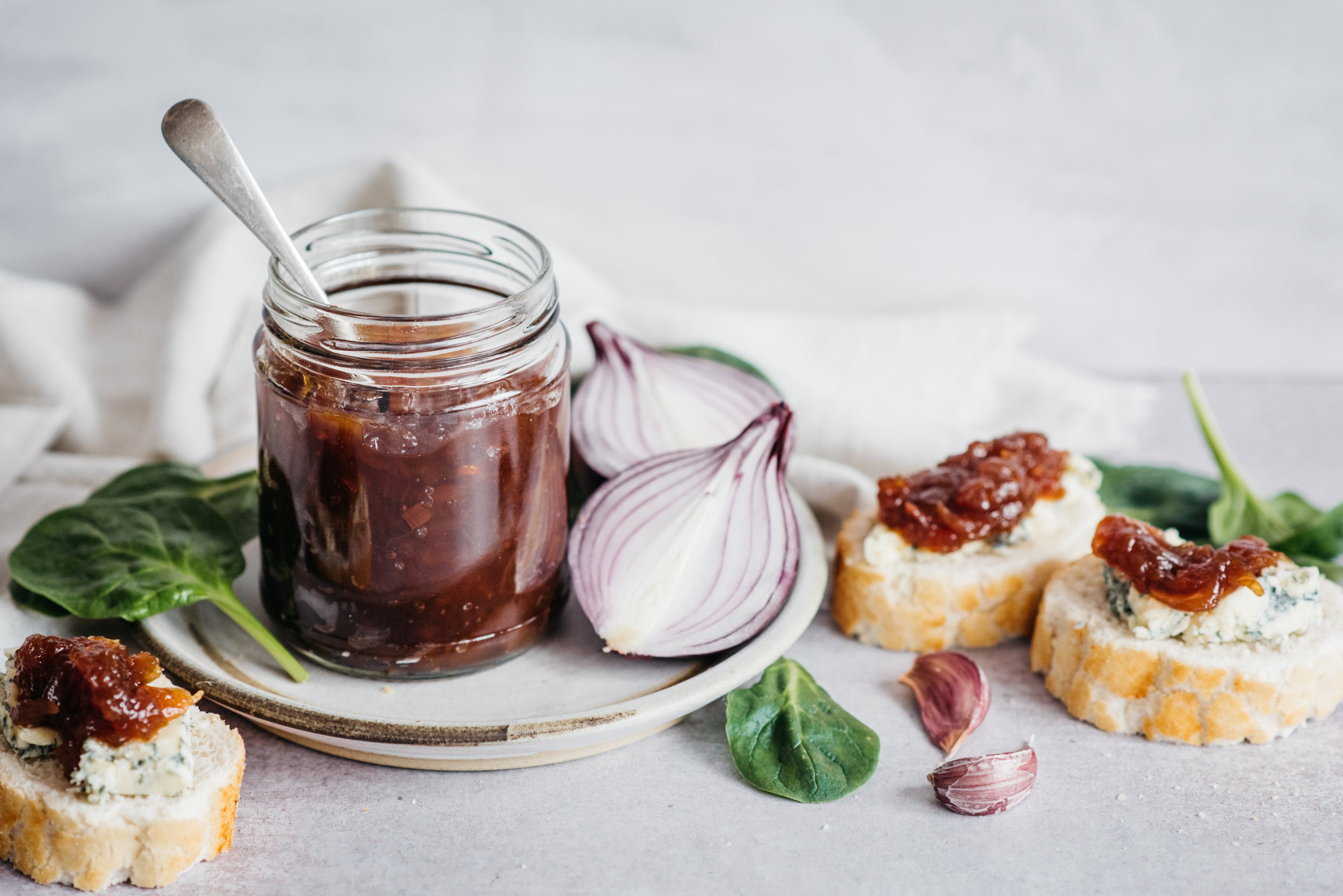 Jar of onion chutney, 3 rounds of bread with cheese and chutney, basil leaves and an onion chopped in half