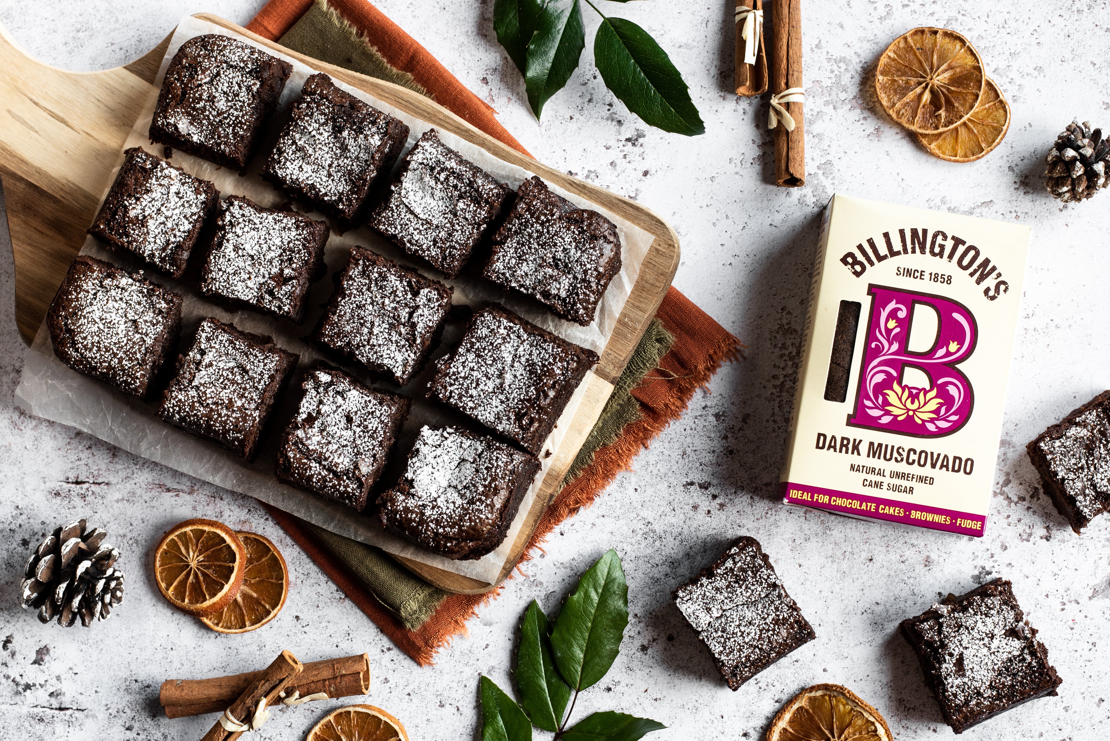 12 chocolate brownies on a wooden board next to a packet of Billington's dark muscovado sugar