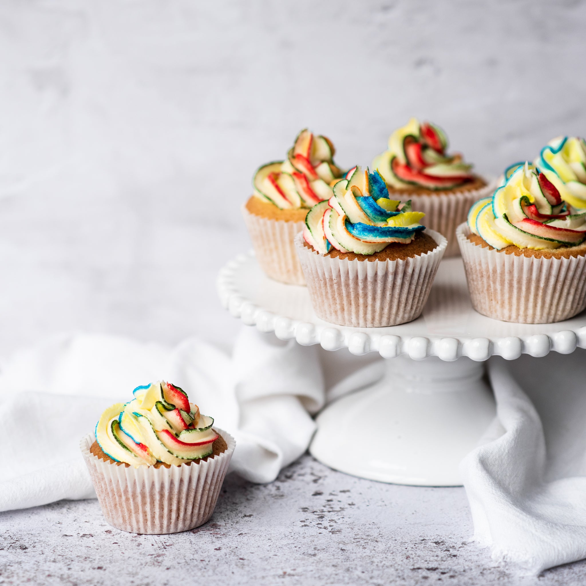 Rainbow cupcakes on a stand with one cupcake upfront