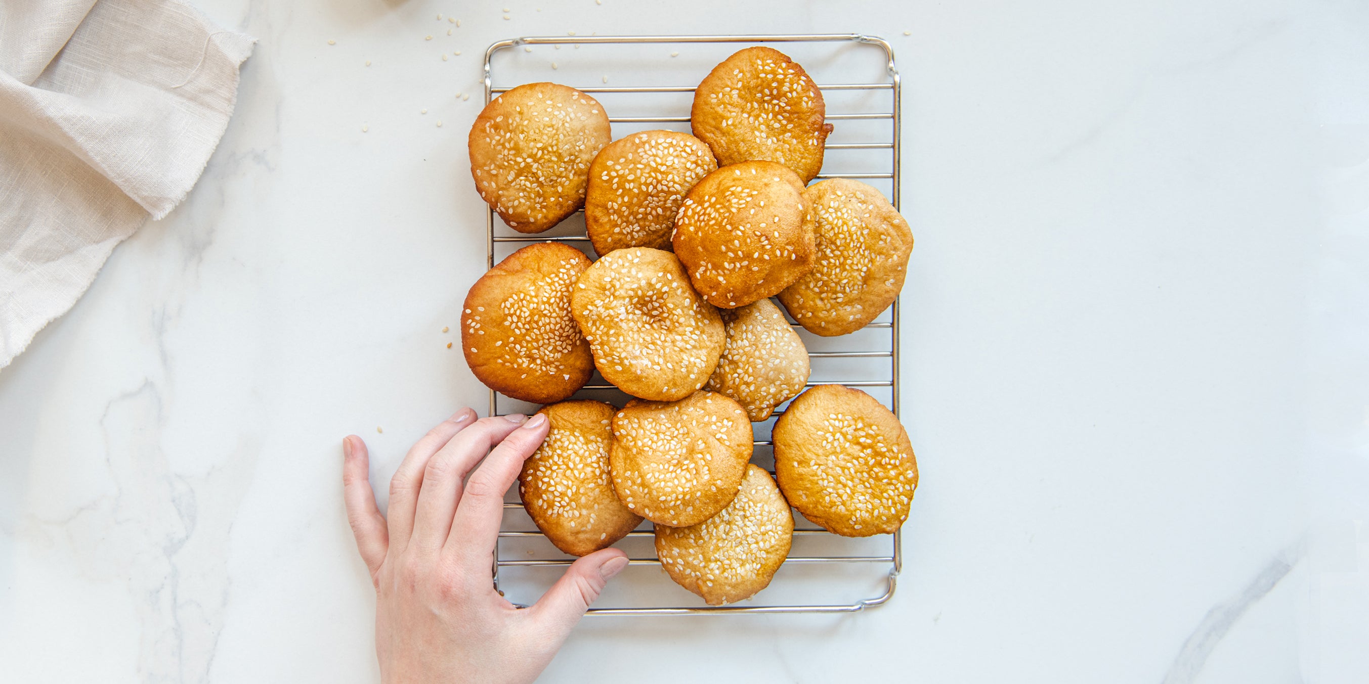 Top view of Bánh Tiêu on a wire cooling rack, with a hand reaching for one