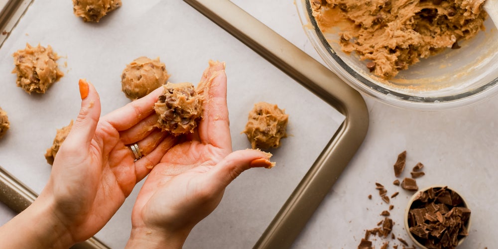Hand rolling out homemade Millie’s chocolate chip cookie dough on a baking tray