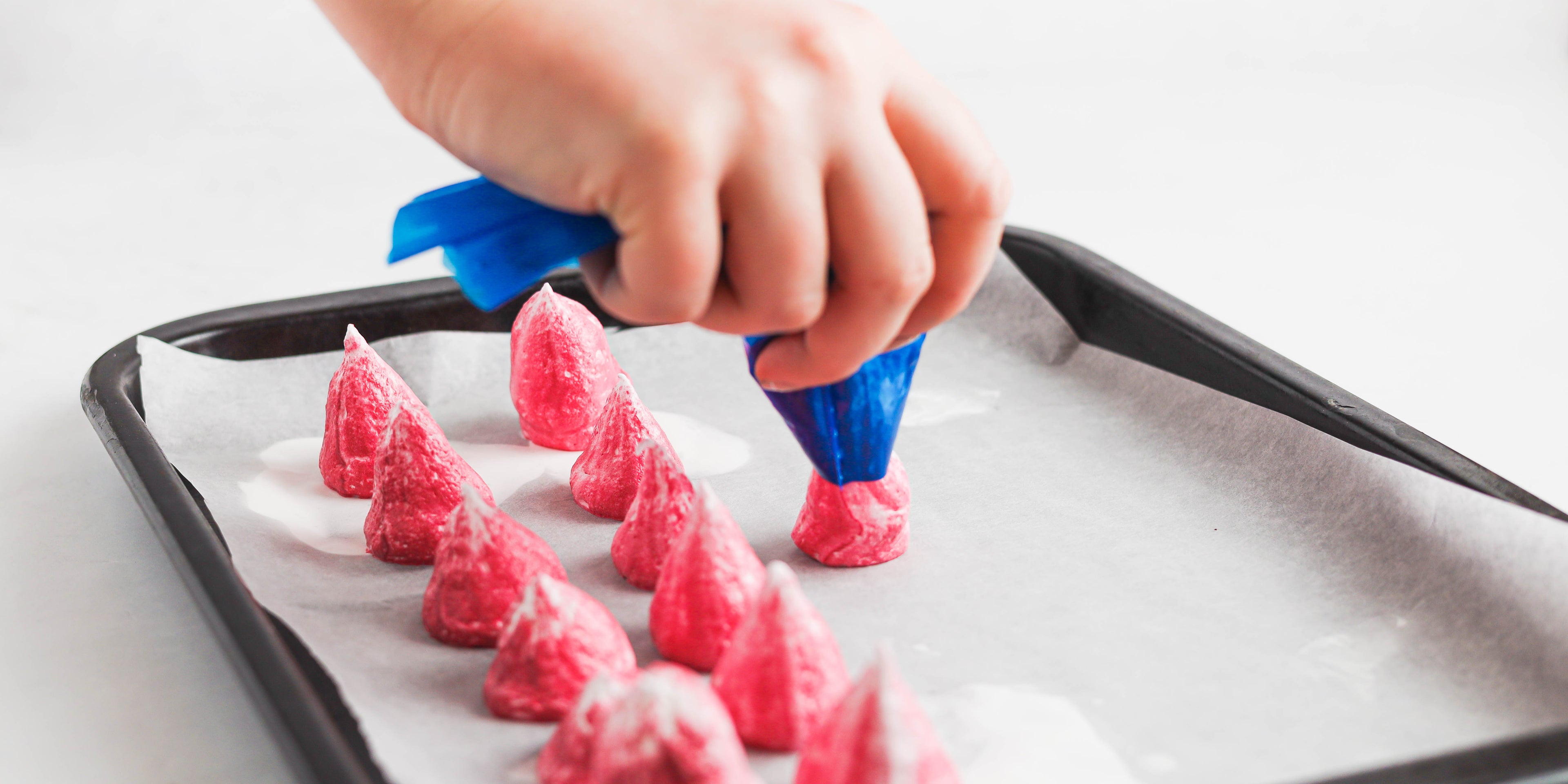 Pink Rainbow Meringues being piped from a piping bag onto baking parchment