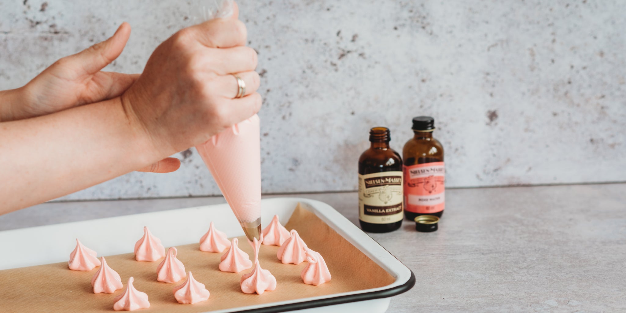 A hand piping buttercream onto baking parchment