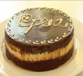 Round opera cake topped with chocolate ganache sitting on a white plate