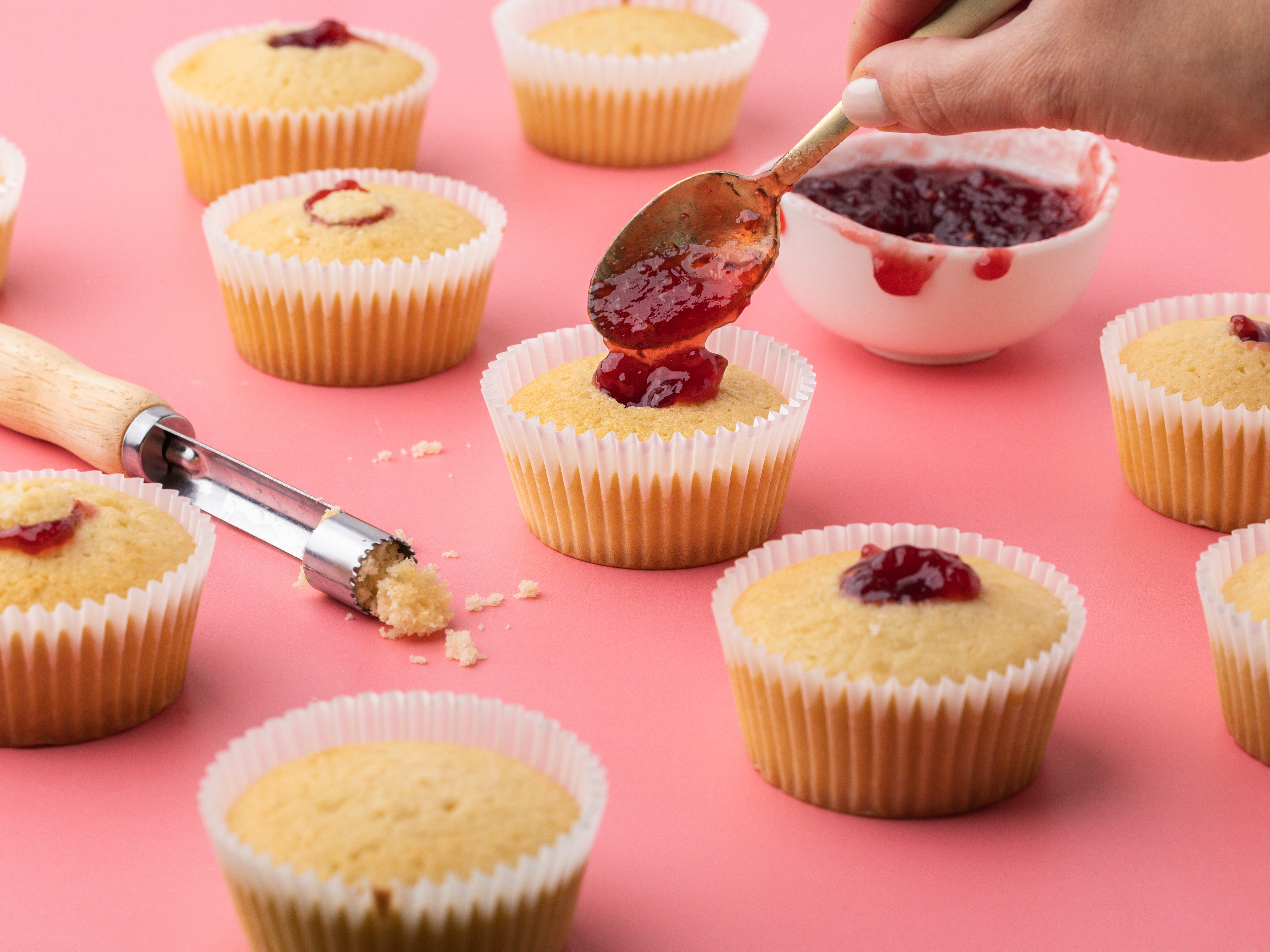 Hand spooning jam into the centre of a cupcake