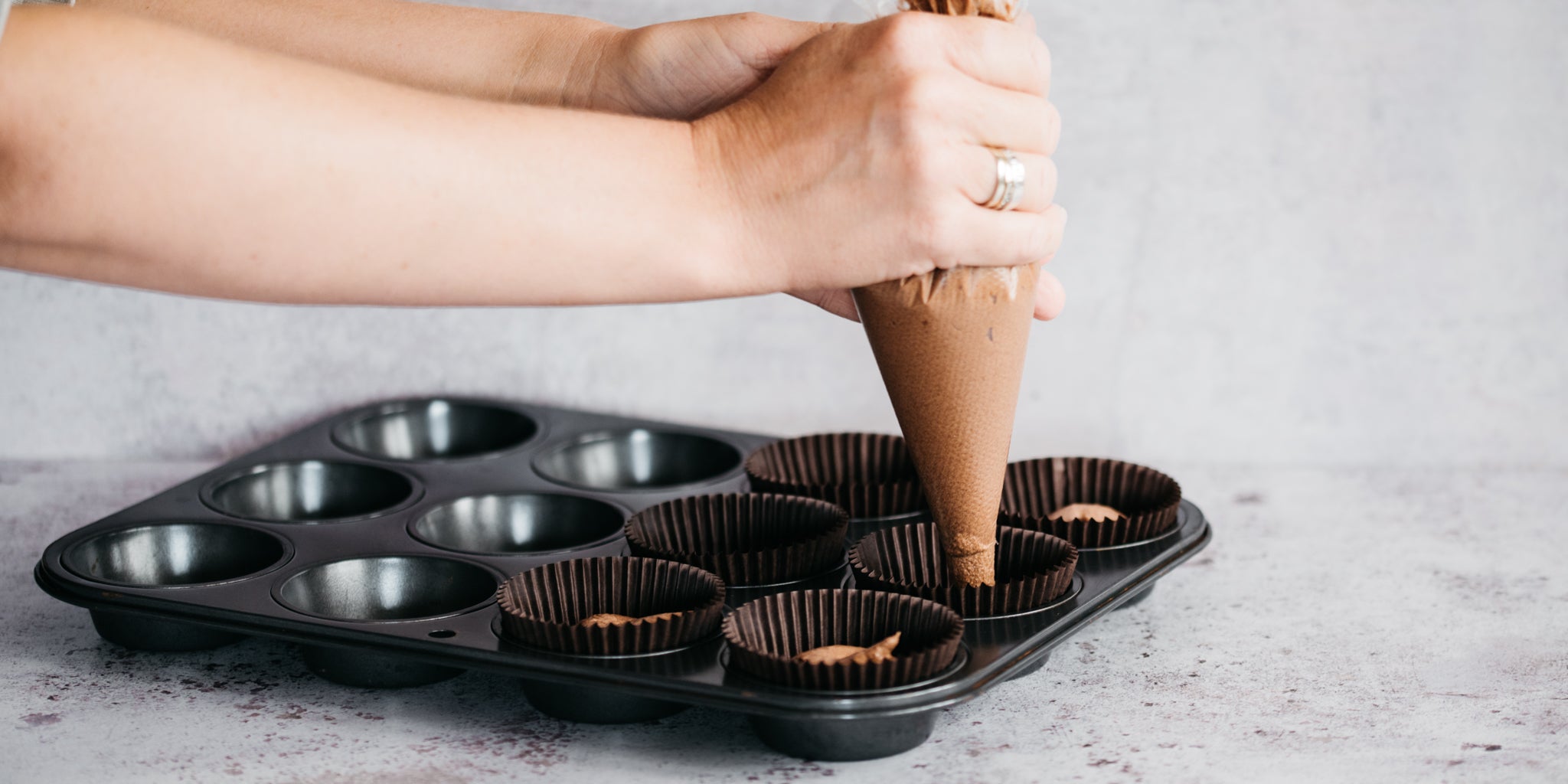 Chocolate & Peppermint Cupcake mixture being piped using a piping bag into cupcake cases ready to bake in a cupcake tray