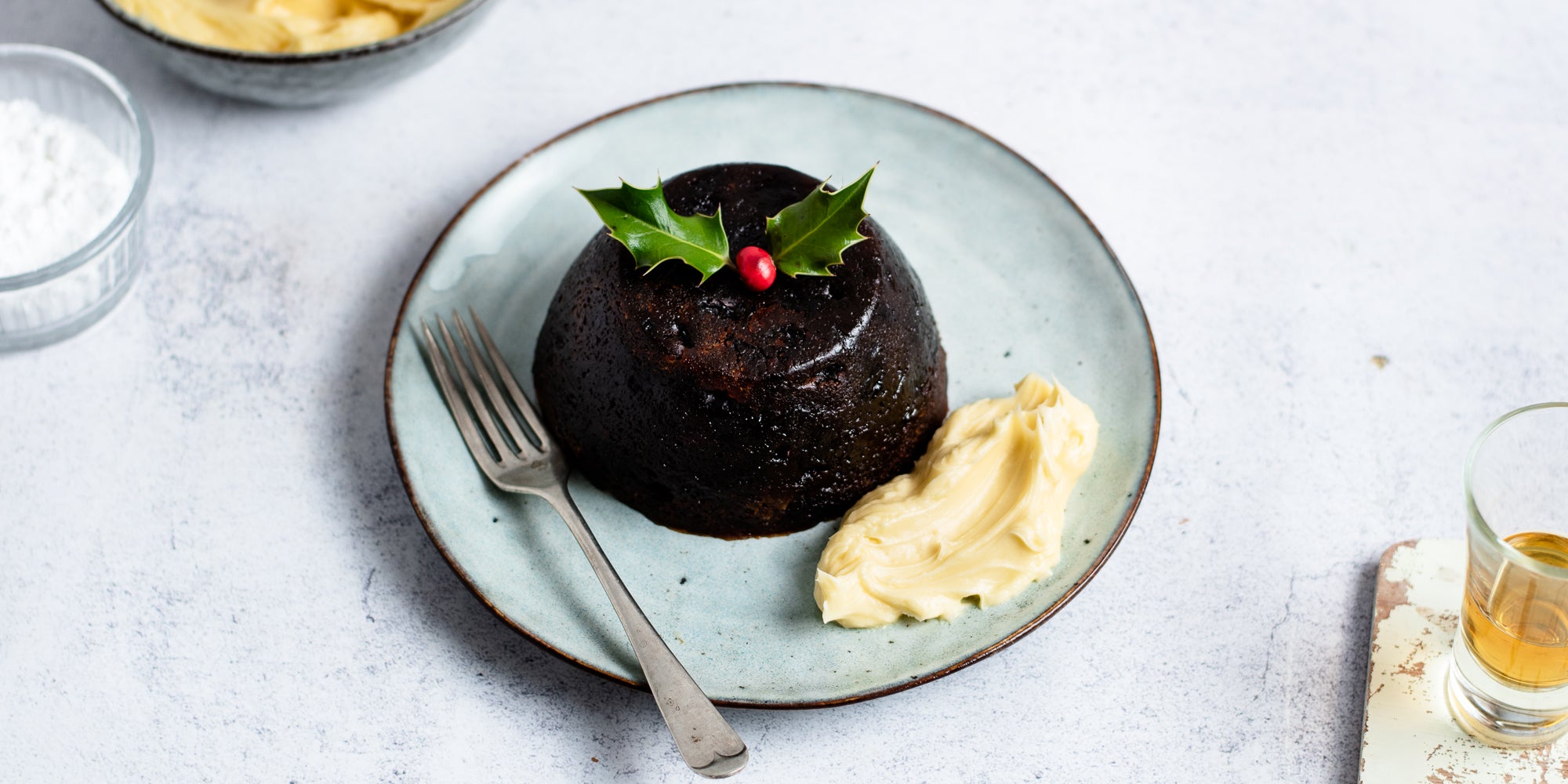 Top view of a christmas pudding next to a dollop of Brandy Butter with a fork ready to eat